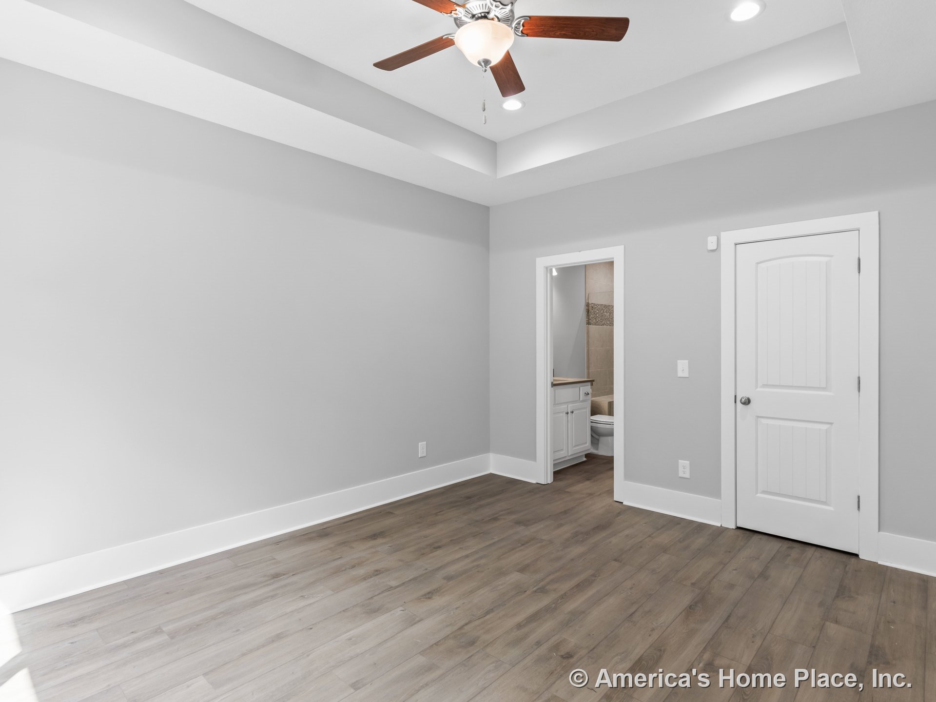 Tray ceiling with recessed lighting and ceiling fan, wood-look plank flooring, white baseboards and trim, en suite bathroom with tile flooring and white cabinetry, white paneled