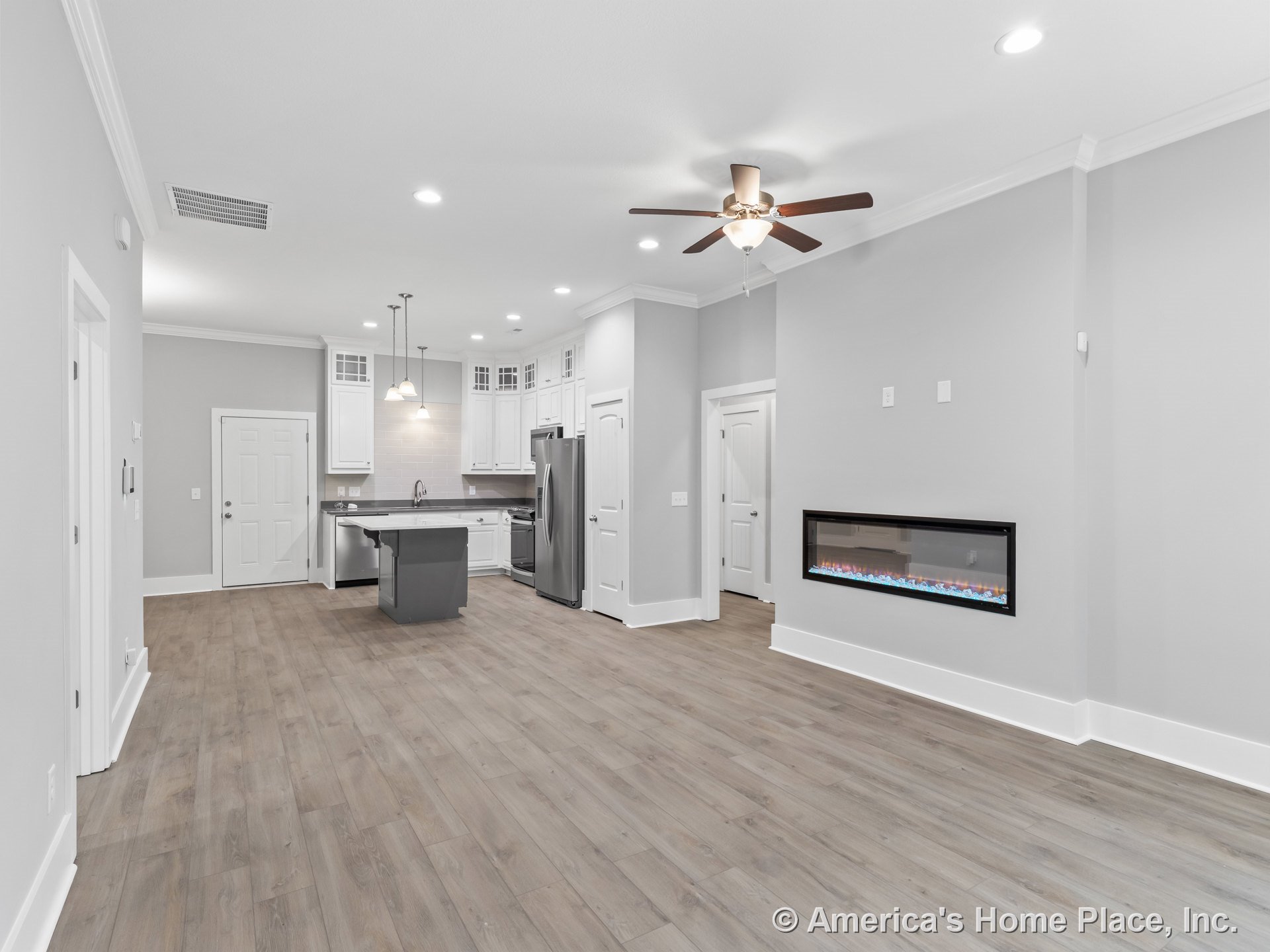 Open concept living area with wood-look flooring, modern linear electric fireplace, kitchen featuring white shaker cabinets, stainless steel appliances, pendant lighting above