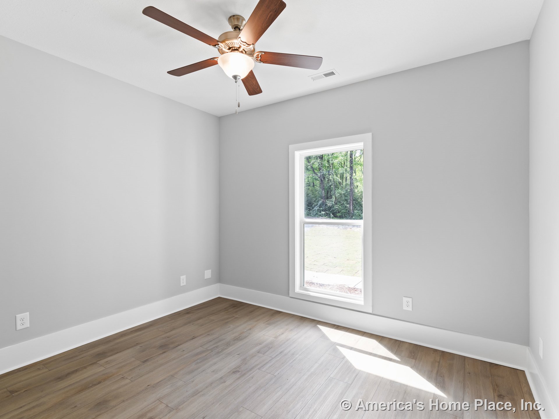 Bedroom with light gray walls, wood-look plank flooring, white baseboard trim, single large window allowing natural light, flat white ceiling, and ceiling fan with integrated light