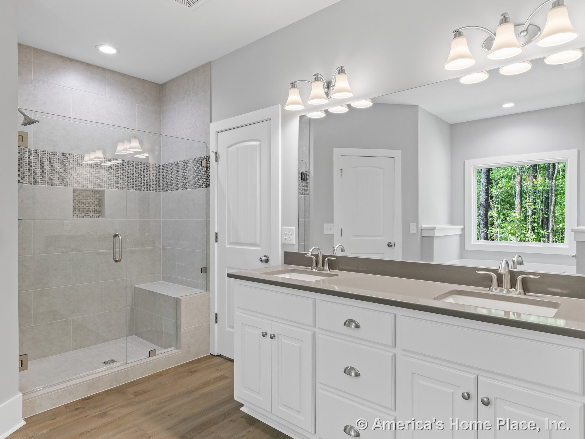 Spacious bathroom with glass-enclosed shower featuring tile accent and built-in bench, double-sink vanity with white shaker cabinets and solid surface countertop, large wall