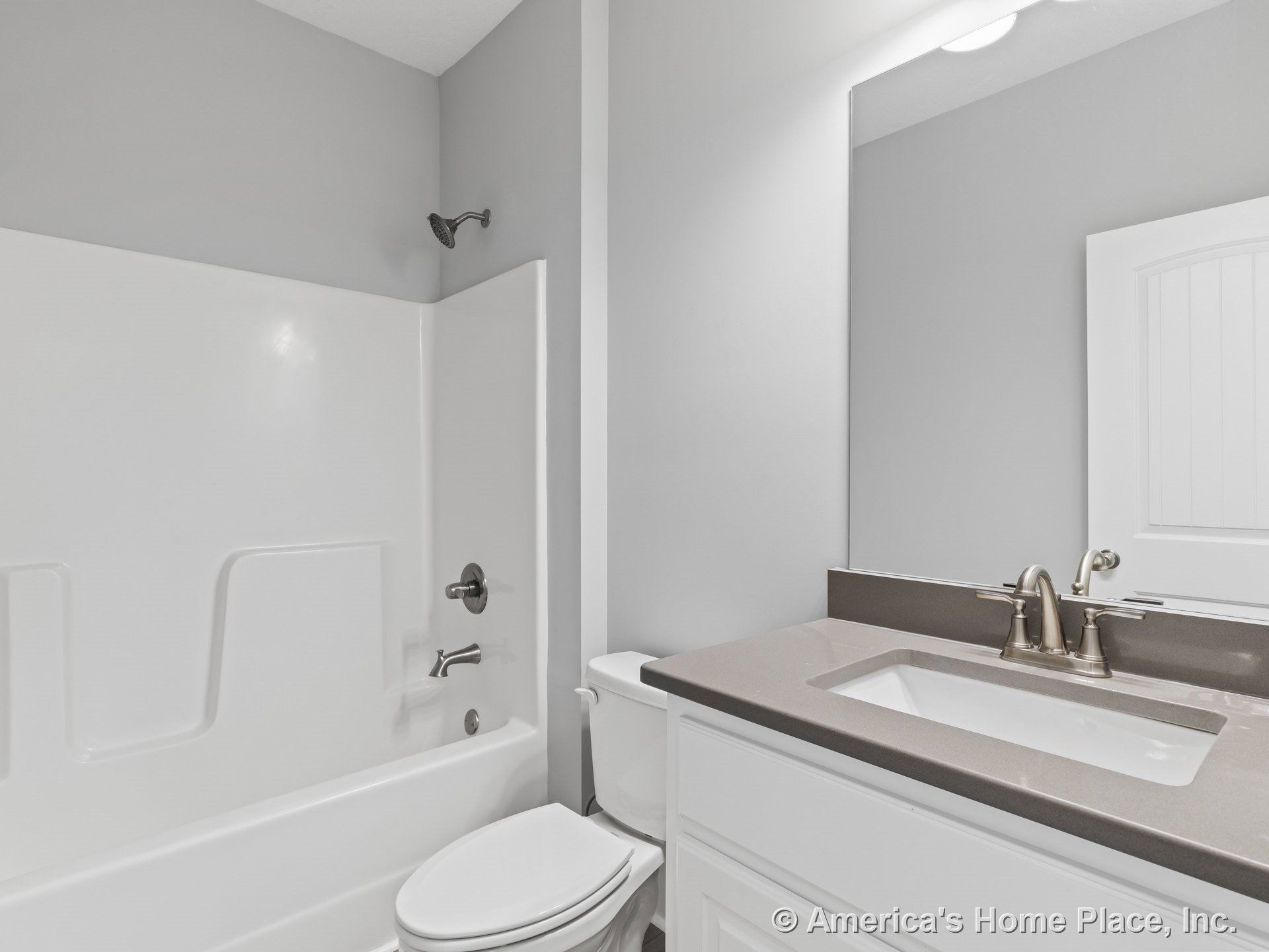 Built-in white bathtub with shower surround, gray solid surface countertop on single-sink white vanity cabinetry, large wall mirror, brushed nickel faucet and fixtures, overhead