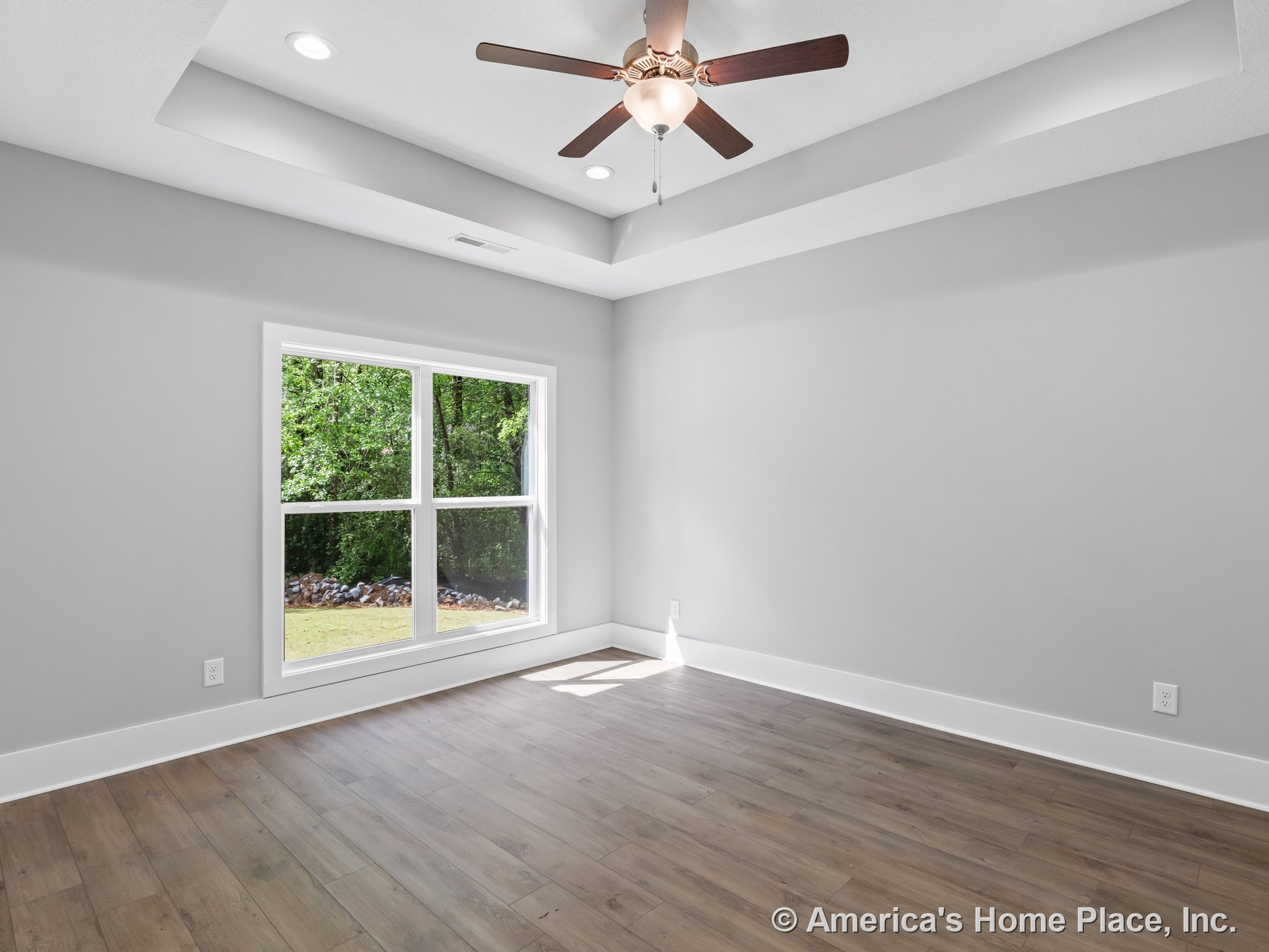Tray ceiling with recessed lighting and ceiling fan, large double window allowing natural light, gray painted walls with wide white baseboards, wood-look plank flooring, modern