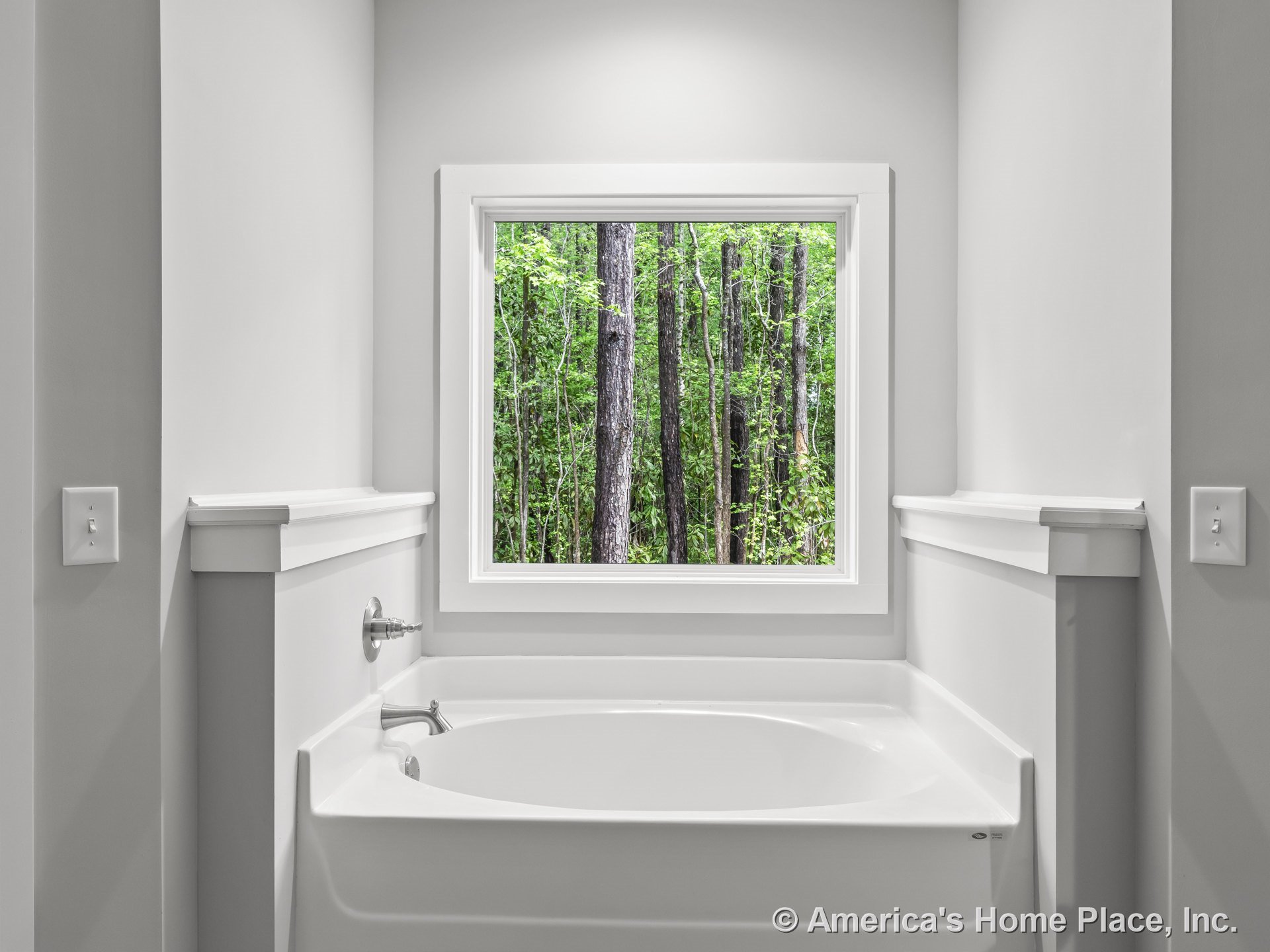 Built-in rectangular soaking tub beneath large window with white trim, gray painted walls, chrome faucet fixtures, raised ledge molding, and abundant natural light.