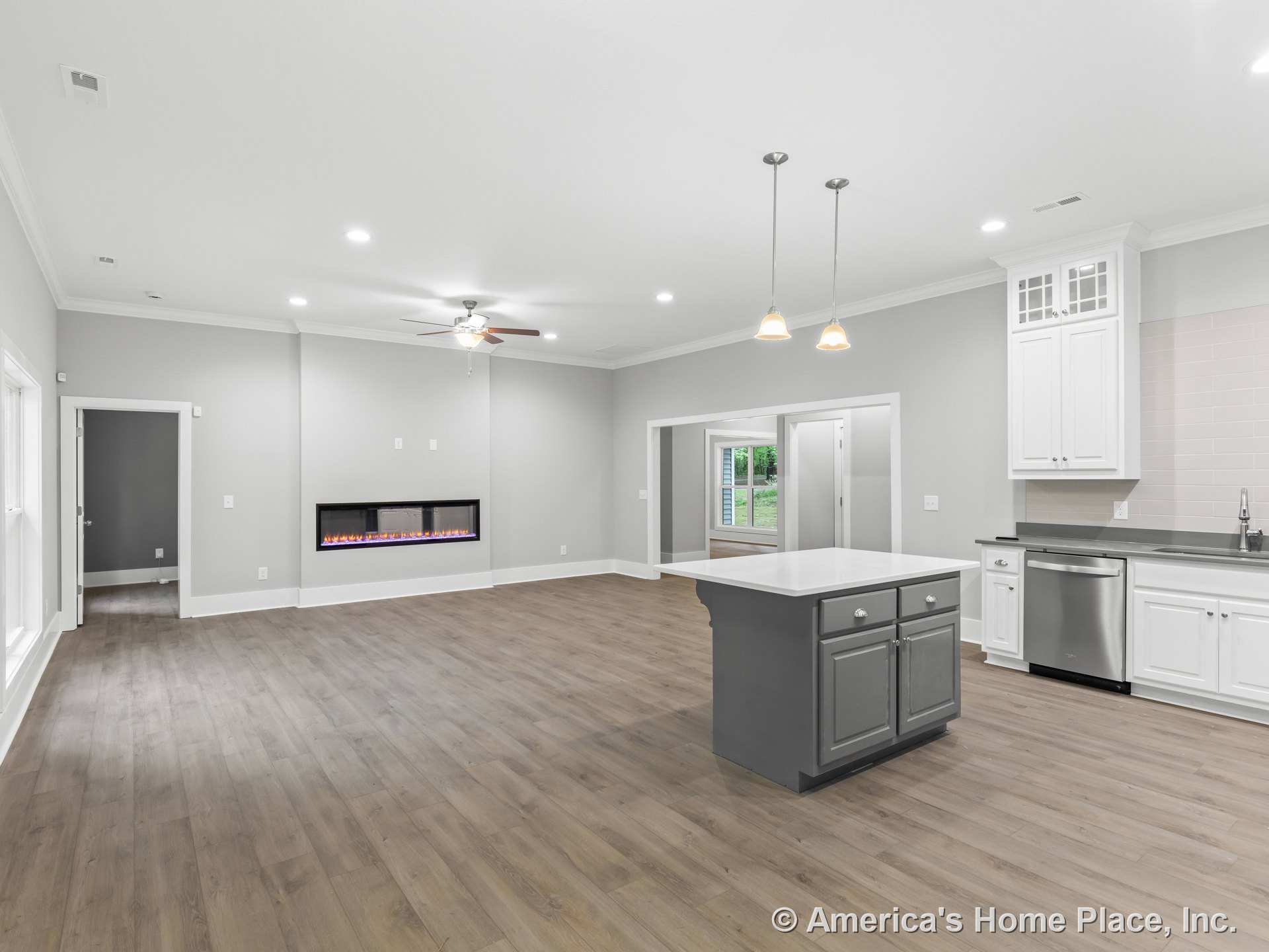 Open-concept living area with modern linear fireplace, white kitchen cabinetry, gray kitchen island topped with white countertop, stainless steel appliances, wood-look flooring
