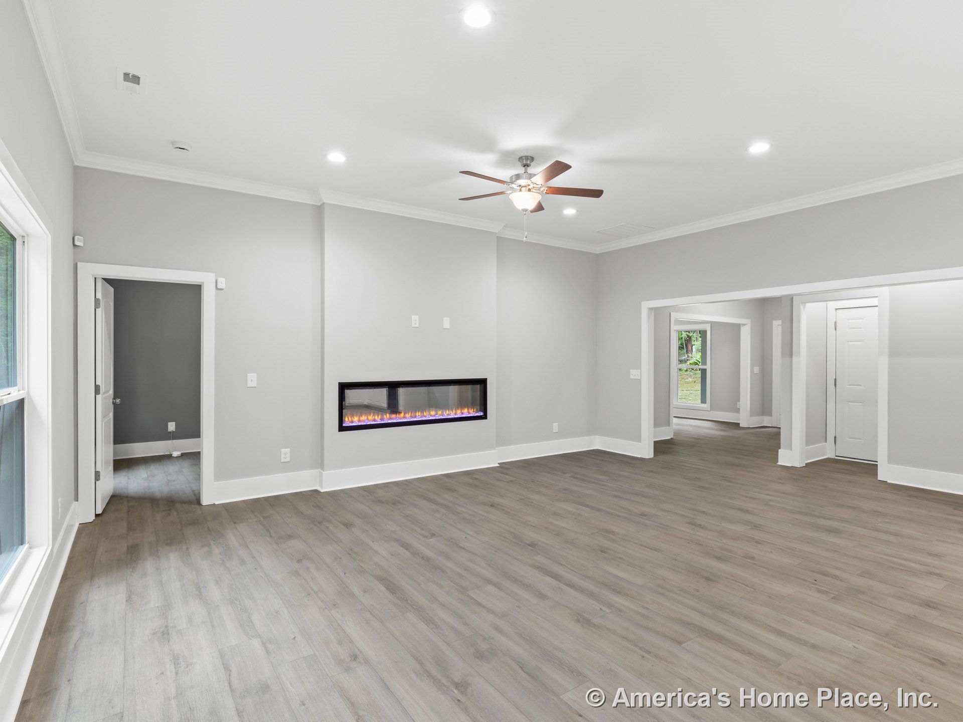 Modern living room with linear wall fireplace, wide plank wood flooring, recessed ceiling lights, large windows, white trim and baseboards, ceiling fan with light, gray walls, and