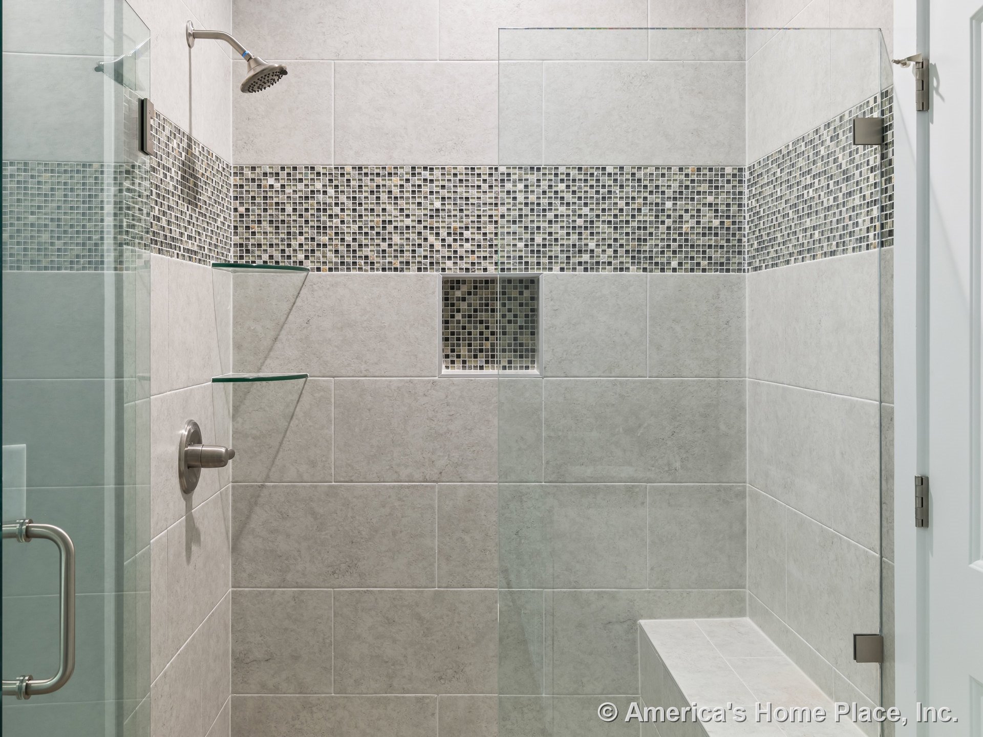 Tiled walk-in shower with mosaic accent strip, built-in niche, glass corner shelves, large format wall tile, shower bench, frameless glass door, and metal fixtures.