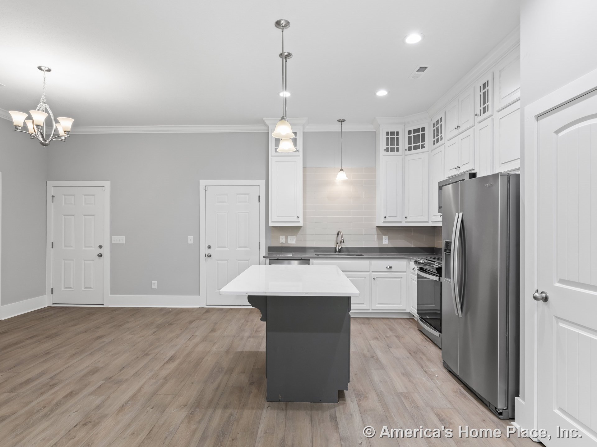 White upper and lower cabinets with crown molding, stainless steel refrigerator and oven, gray subway tile backsplash, central island with quartz countertops, pendant and recessed