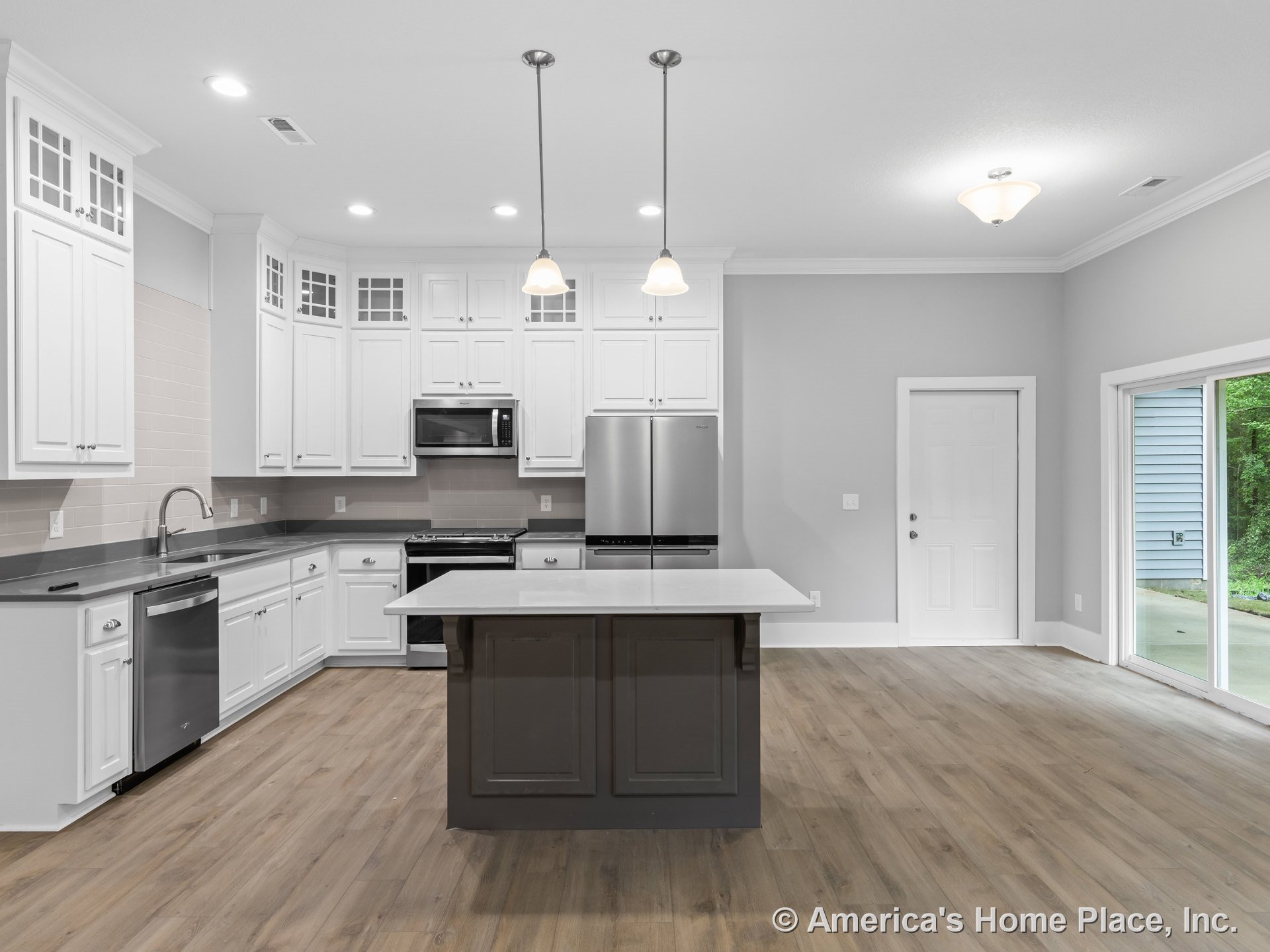 White kitchen cabinetry with glass upper inserts, gray solid surface countertops, tile backsplash, stainless steel appliances, central island with dark finish, pendant and flush