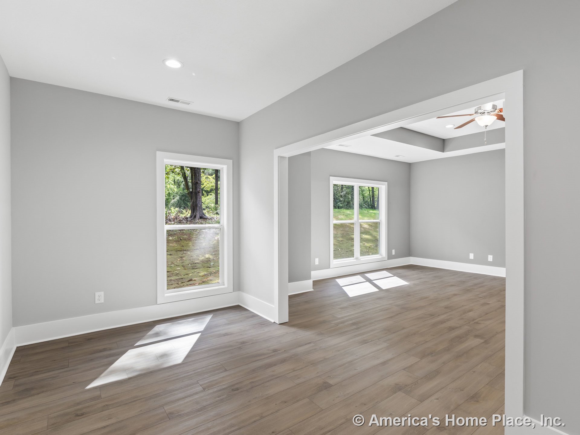 Open concept living area with expansive double-pane windows, light wood plank flooring, tray ceiling featuring recessed lighting and ceiling fan, white baseboard trim, and neutral