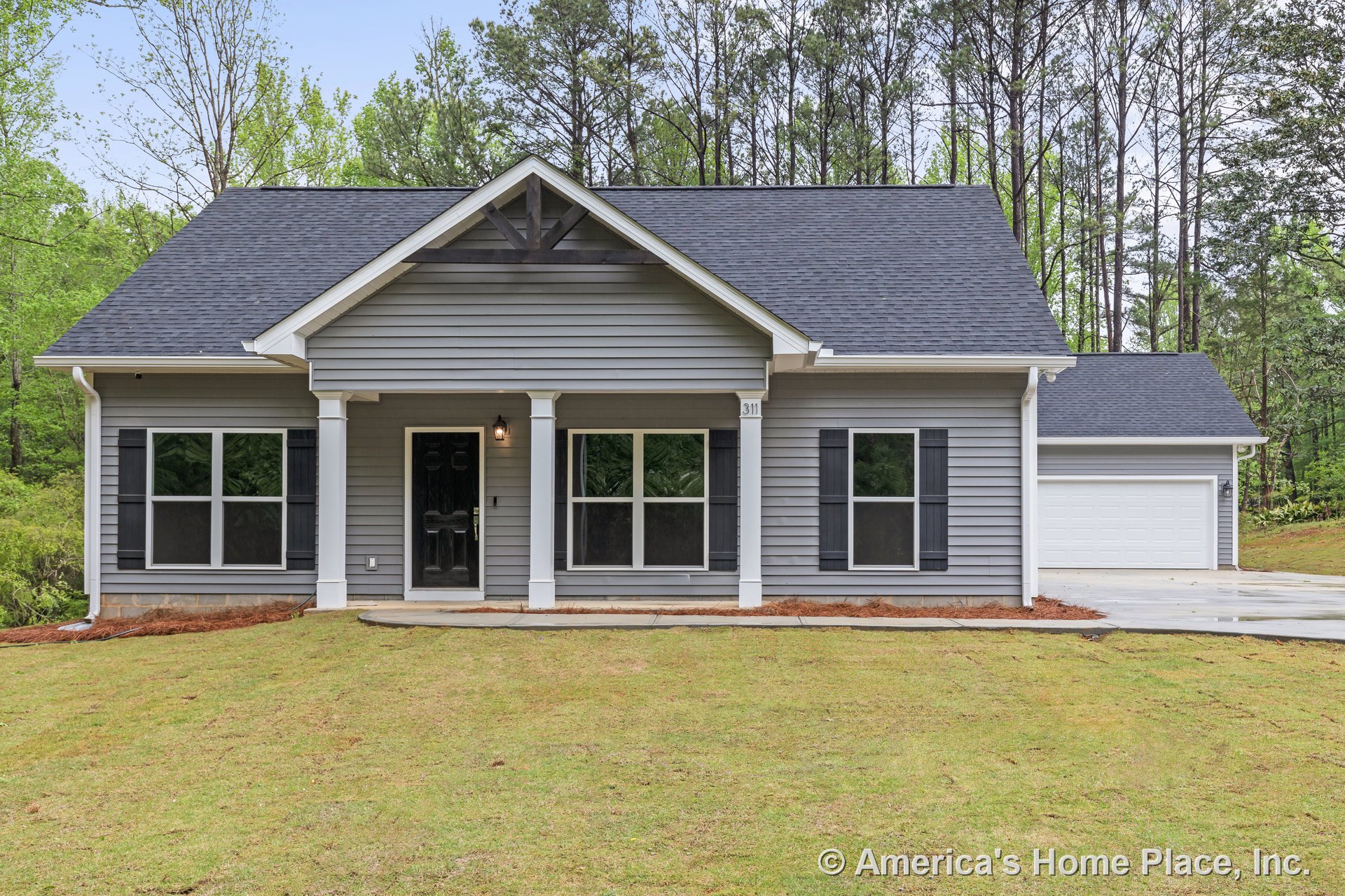 Gray vinyl siding exterior with covered front porch supported by white columns, black front door, double-pane windows with black shutters, detached two-car garage, paved driveway