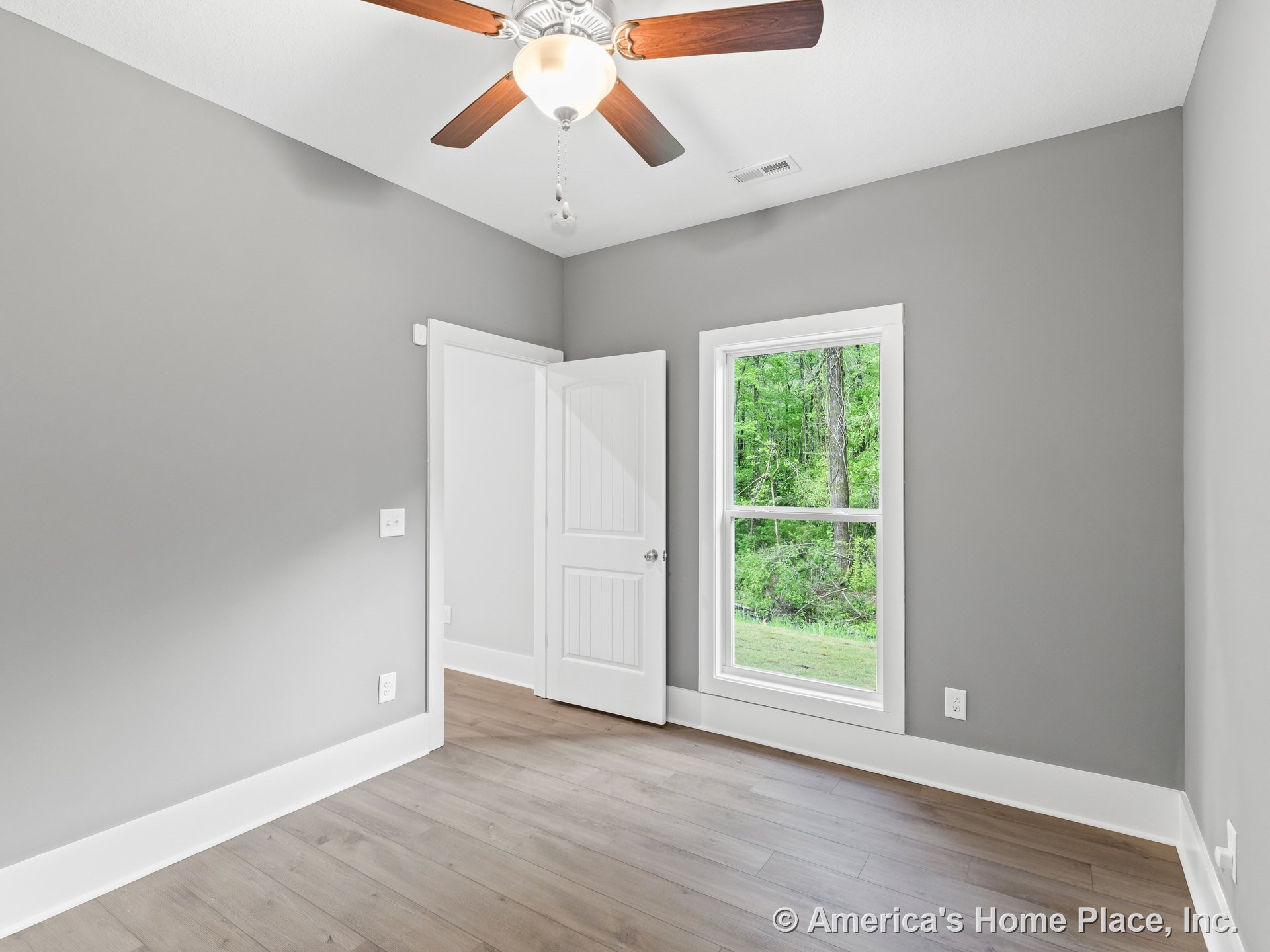 Bedroom with gray walls, white baseboards and door trim, single large window allowing natural light, wood-look plank flooring, ceiling fan with light fixture, and paneled white
