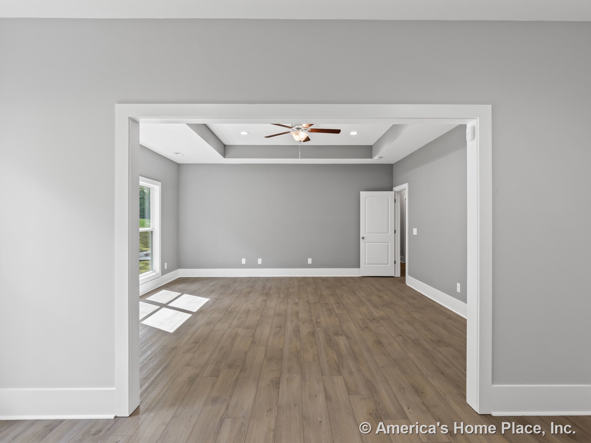 Tray ceiling with recessed lighting and ceiling fan, wood-look plank flooring, large window with white trim, white baseboards and door trim, paneled interior door, gray walls, open