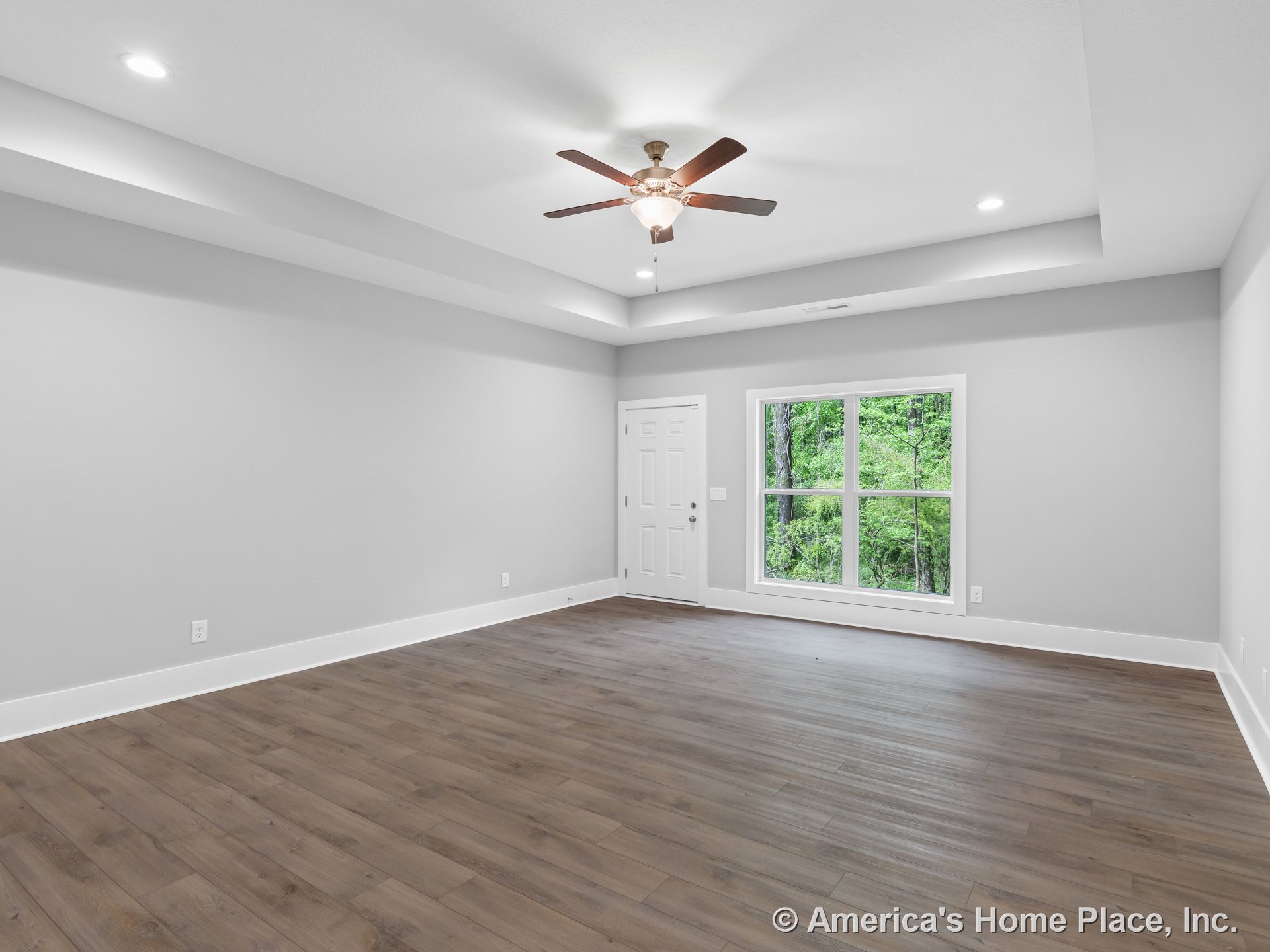 Tray ceiling with recessed lighting and ceiling fan, large double window with white trim, wood-look plank flooring, white baseboards, entry door with decorative trim, neutral wall