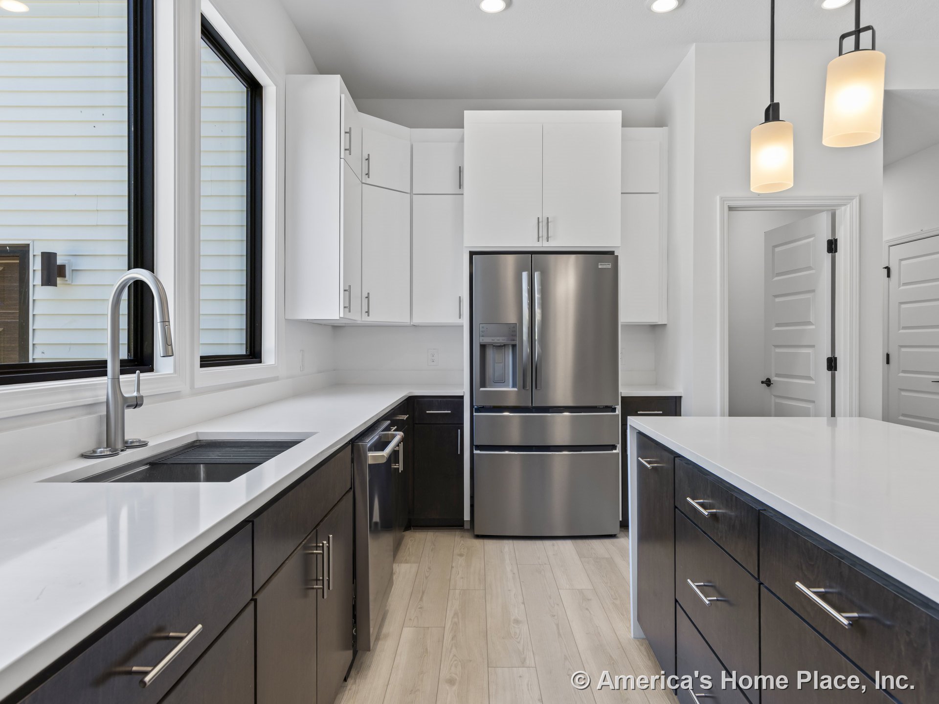 White quartz countertops and dark flat panel lower cabinetry with stainless steel appliances, white upper cabinets, large windows above the sink, modern pendant lighting, light