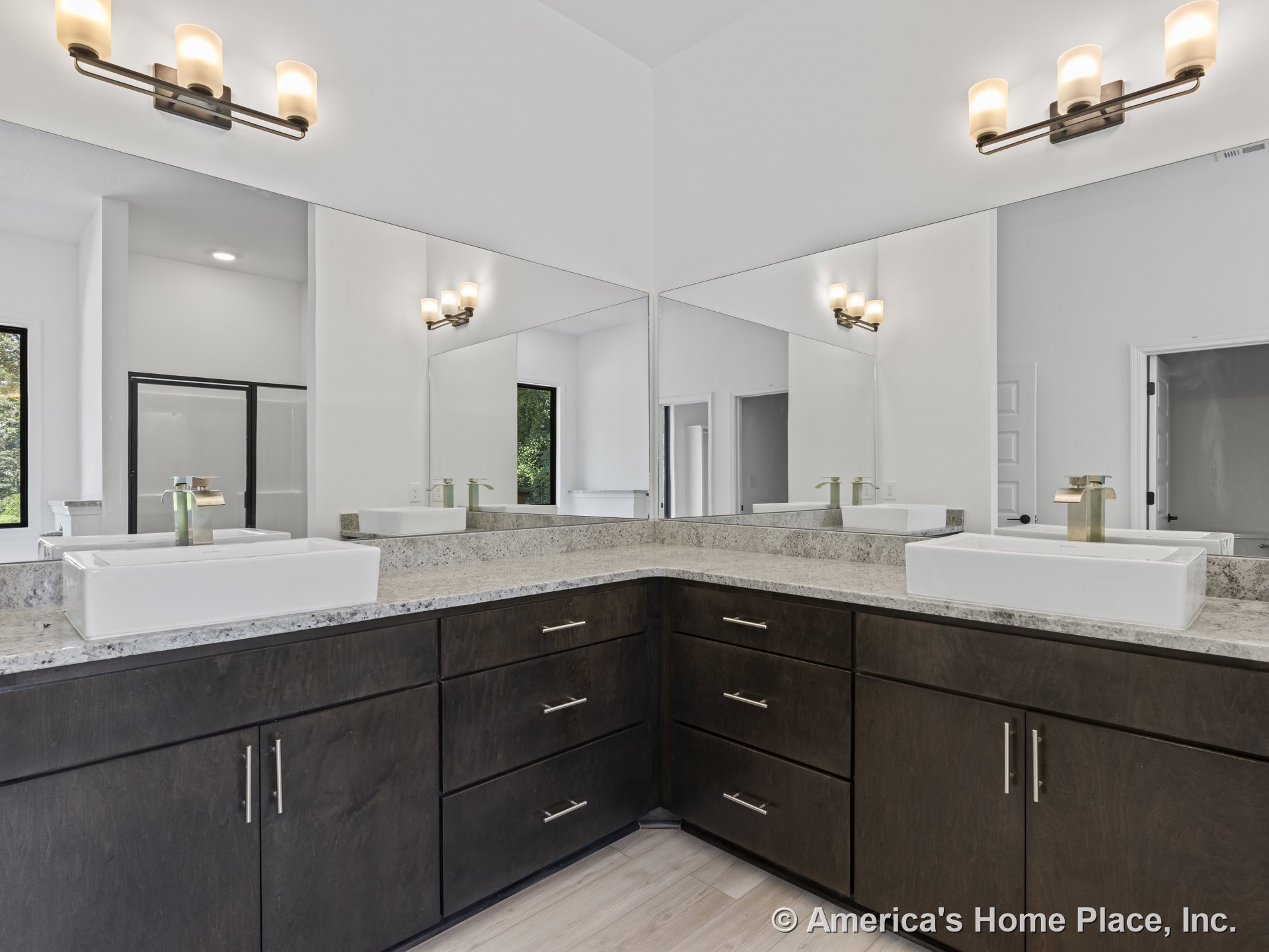 Double vanity with dark wood cabinets and granite countertops, large wall mirrors above sinks, modern light fixtures, light wood flooring, window with trim.