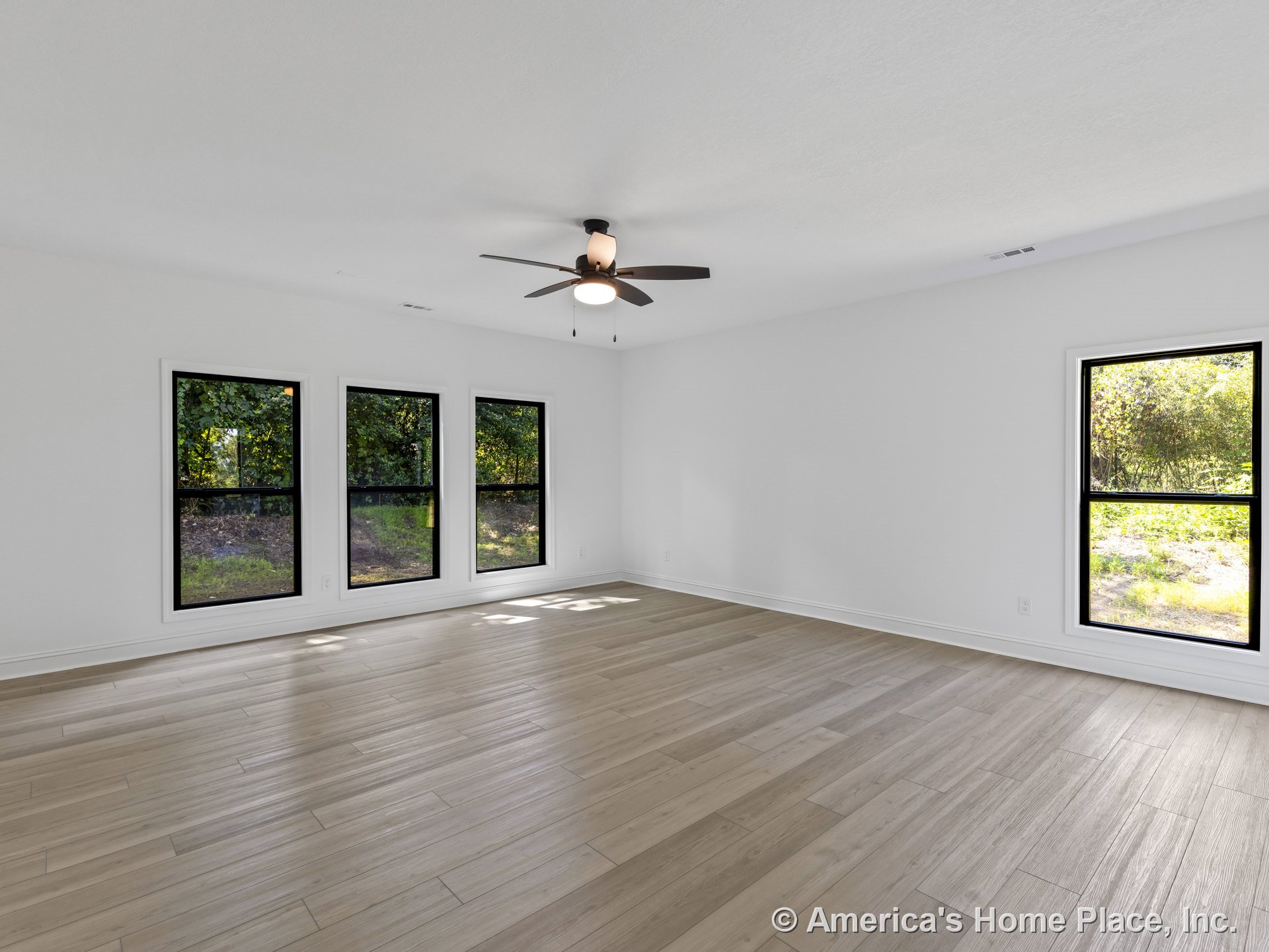 Spacious living room with light wood-look tile flooring, four large black-trim windows, white walls, flat white ceiling, ceiling fan with light, and minimalist white baseboards.