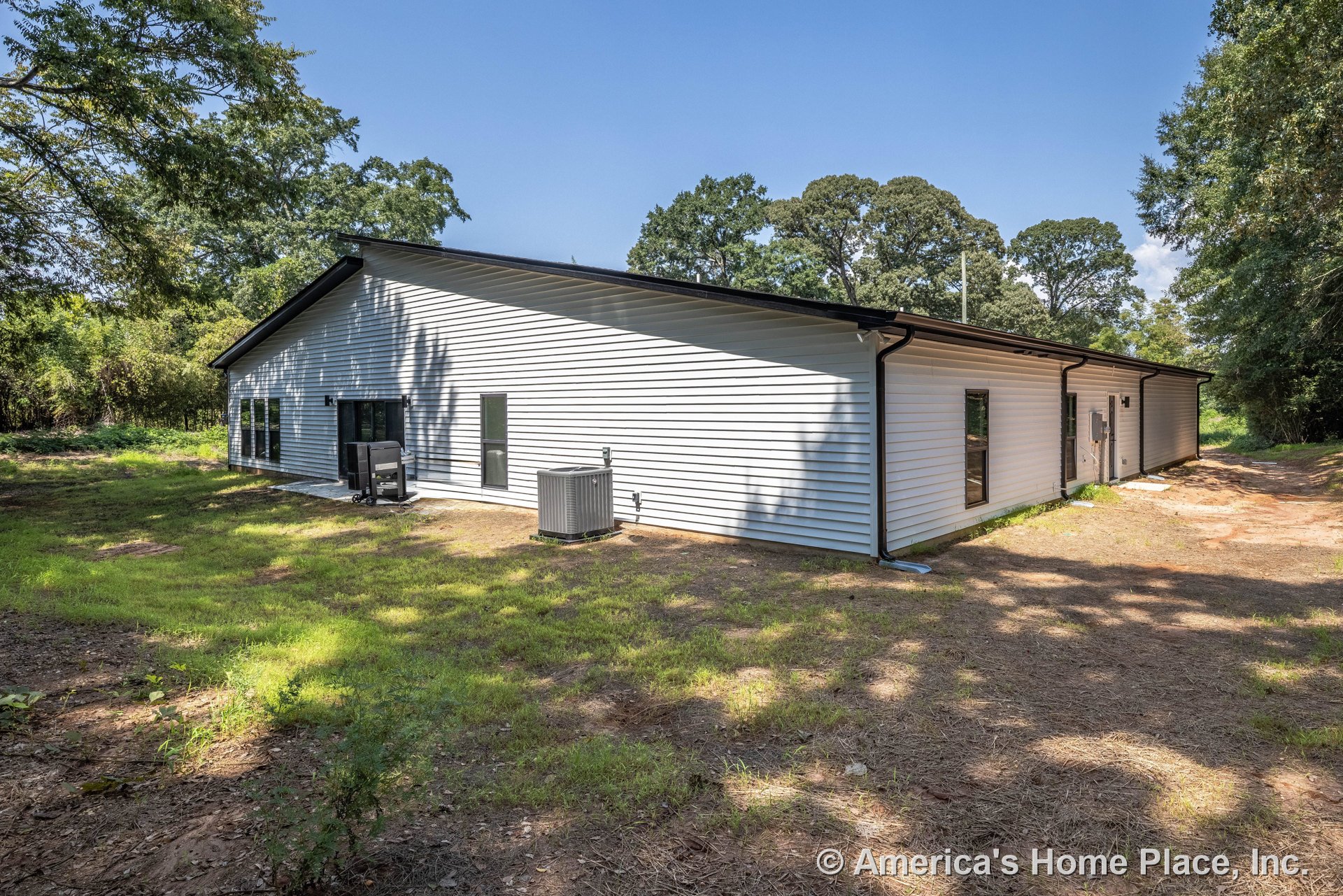 Light-colored horizontal vinyl siding exterior with black-trimmed rectangular windows, sloped roof, exterior HVAC unit, and side entry door.