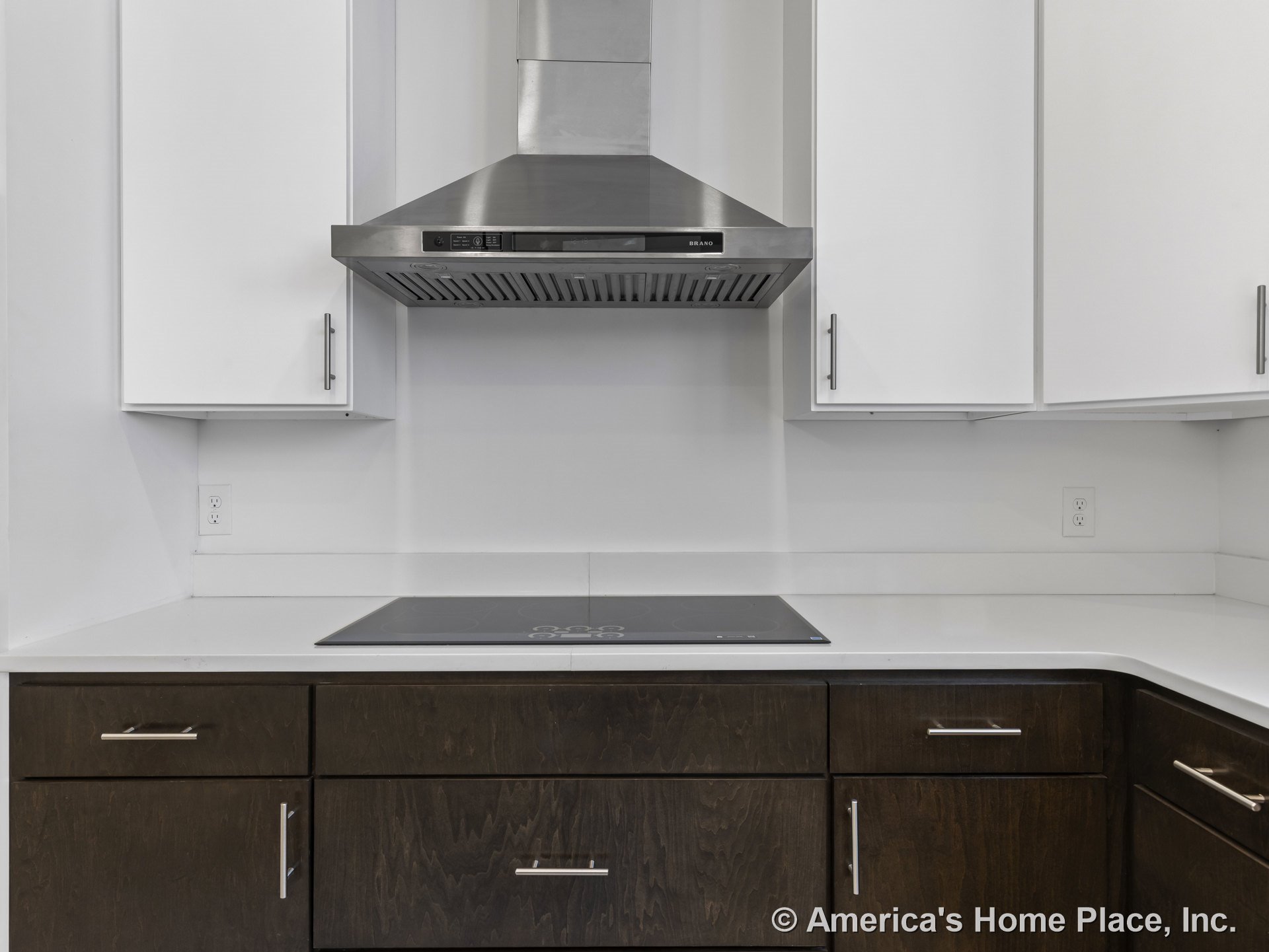 Stainless steel range hood above smooth electric cooktop, white upper cabinets paired with dark wood lower cabinetry, white quartz countertops, and sleek metal cabinet pulls in a