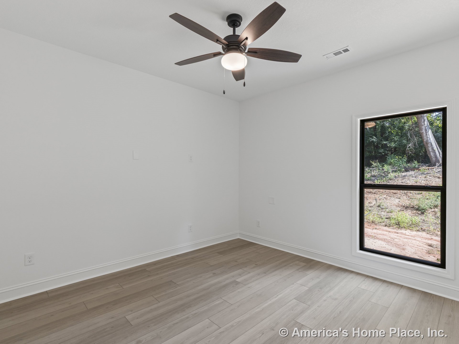 Light wood plank flooring, white walls with baseboard trim, large black-trim single window allowing natural light, ceiling fan with integrated lighting, minimalist modern finishes.