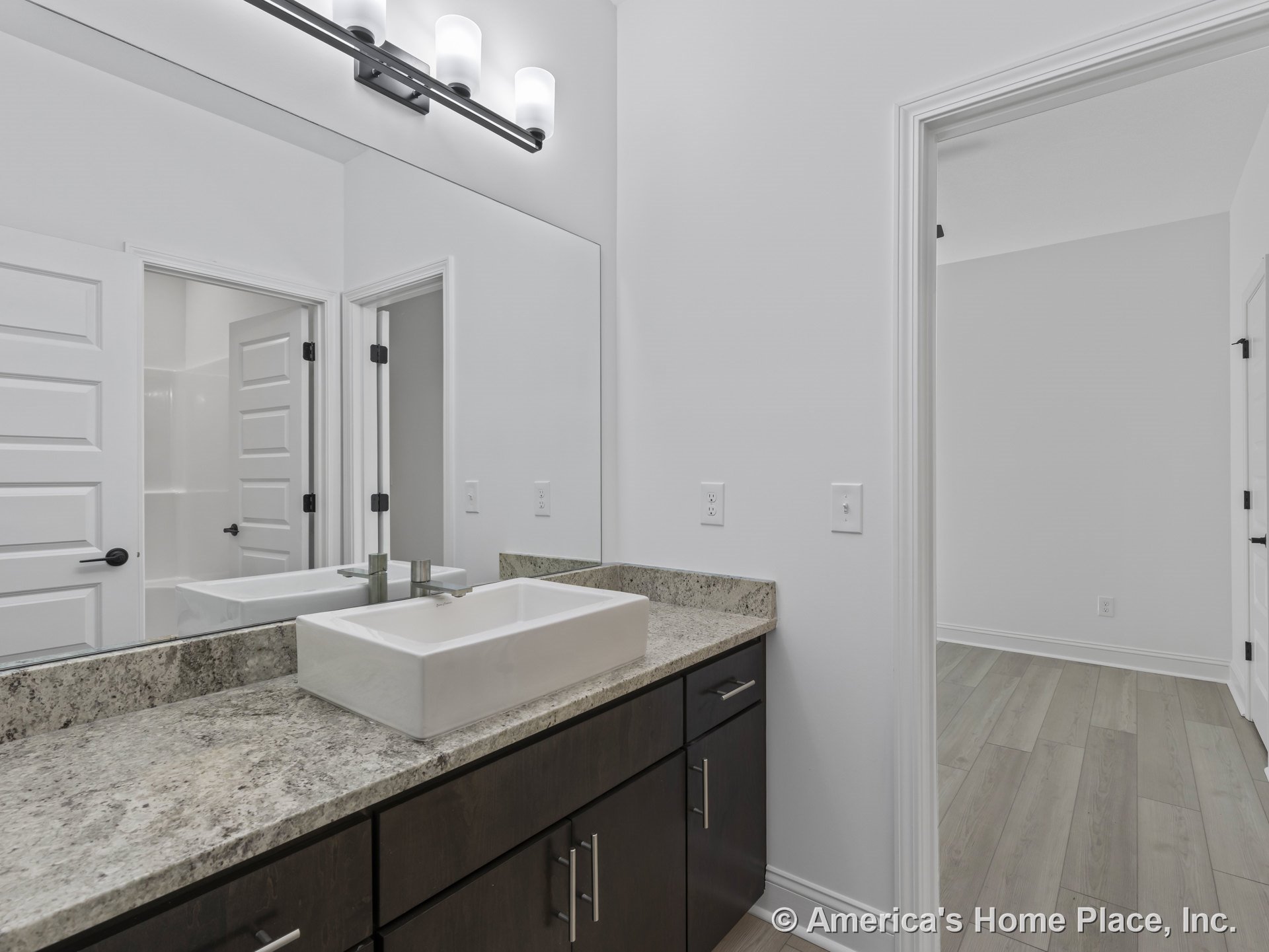 Rectangular vessel sink atop granite countertop with dark wood cabinetry, large wall mirror, modern vanity light fixture, and white paneled doors.