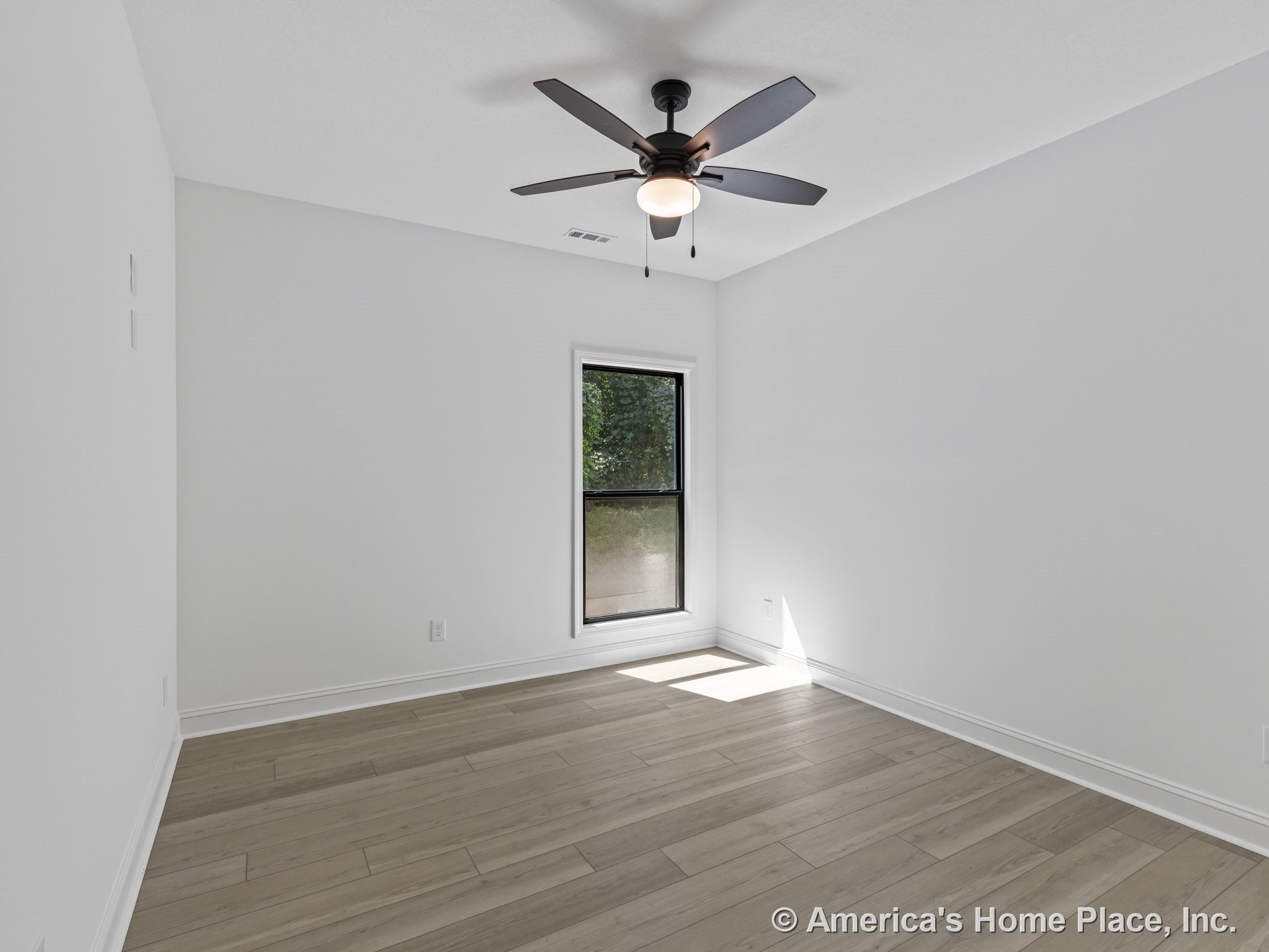 Bedroom with light wood plank flooring, white painted walls, black framed single window, ceiling fan with integrated light, simple baseboard trim, and natural light illuminating