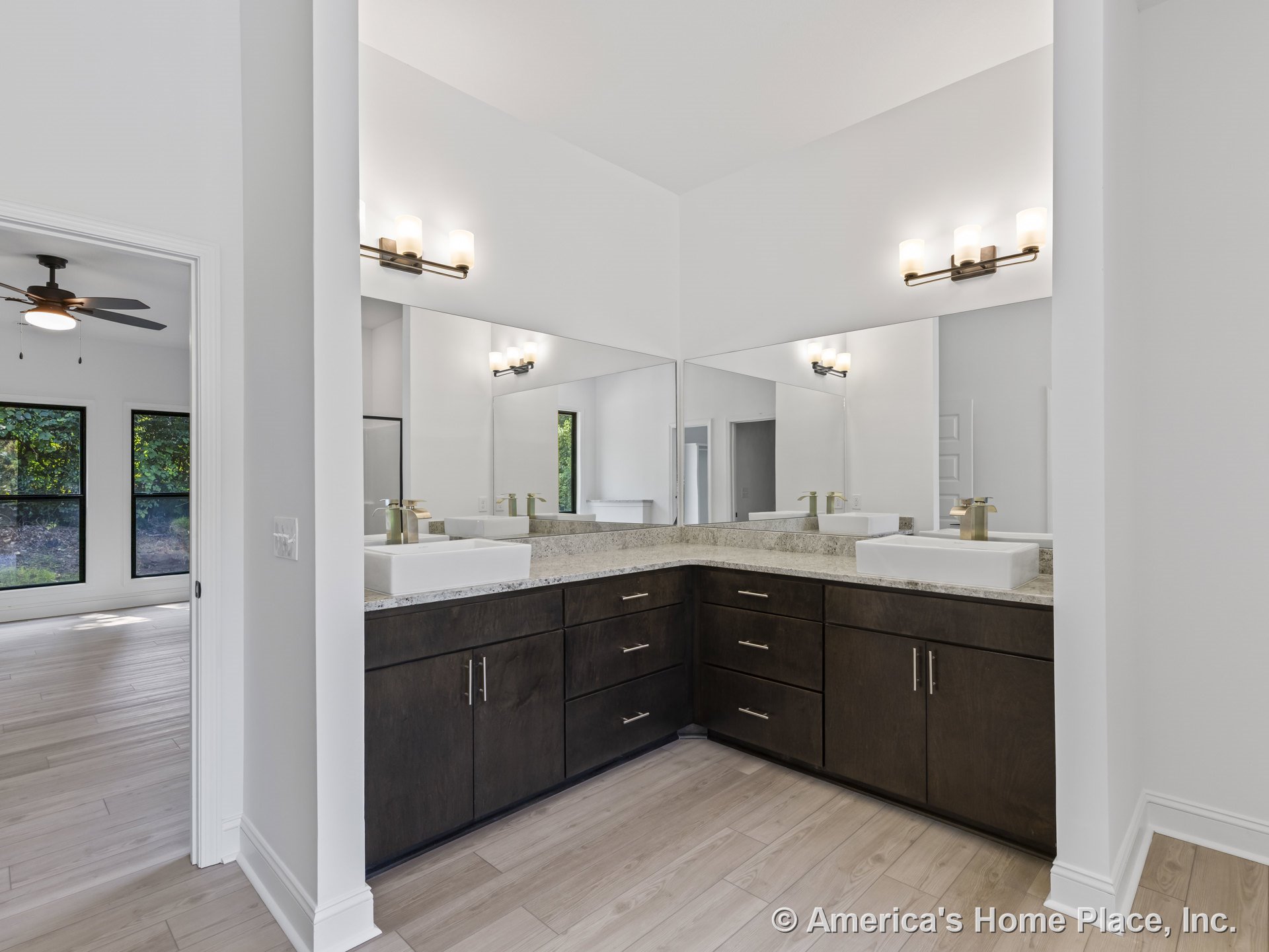 Dark wood cabinetry with granite countertops, dual vessel sinks, expansive wall mirrors, modern wall-mounted lighting fixtures, and light wood flooring in a double vanity bathroom.