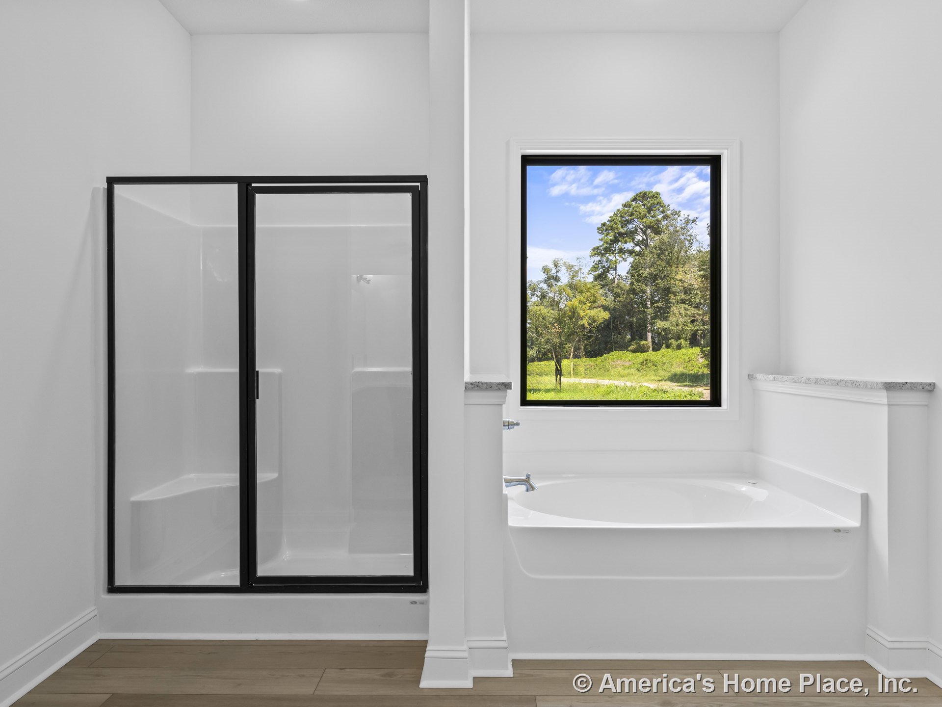 Glass-enclosed shower and built-in bathtub positioned beneath a large picture window, white walls, wood-look flooring, and granite ledge trim create a modern bathroom with abundant