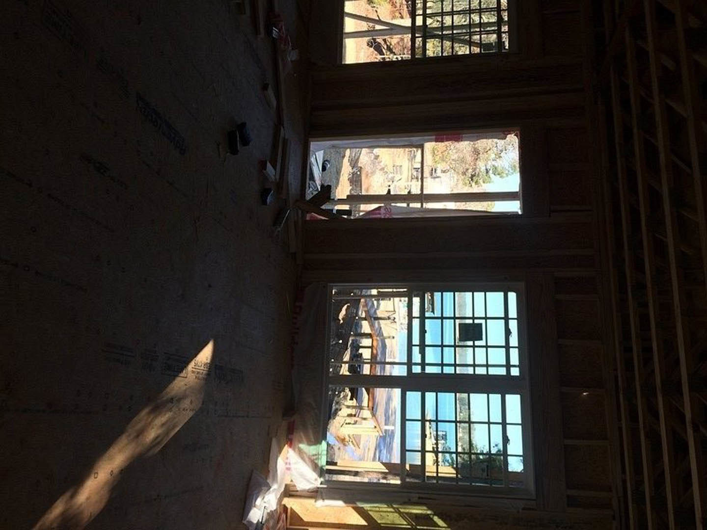 Sunlit room with large windows, light wood flooring, and white walls; partial shadow cast on the floor, modern fixtures visible