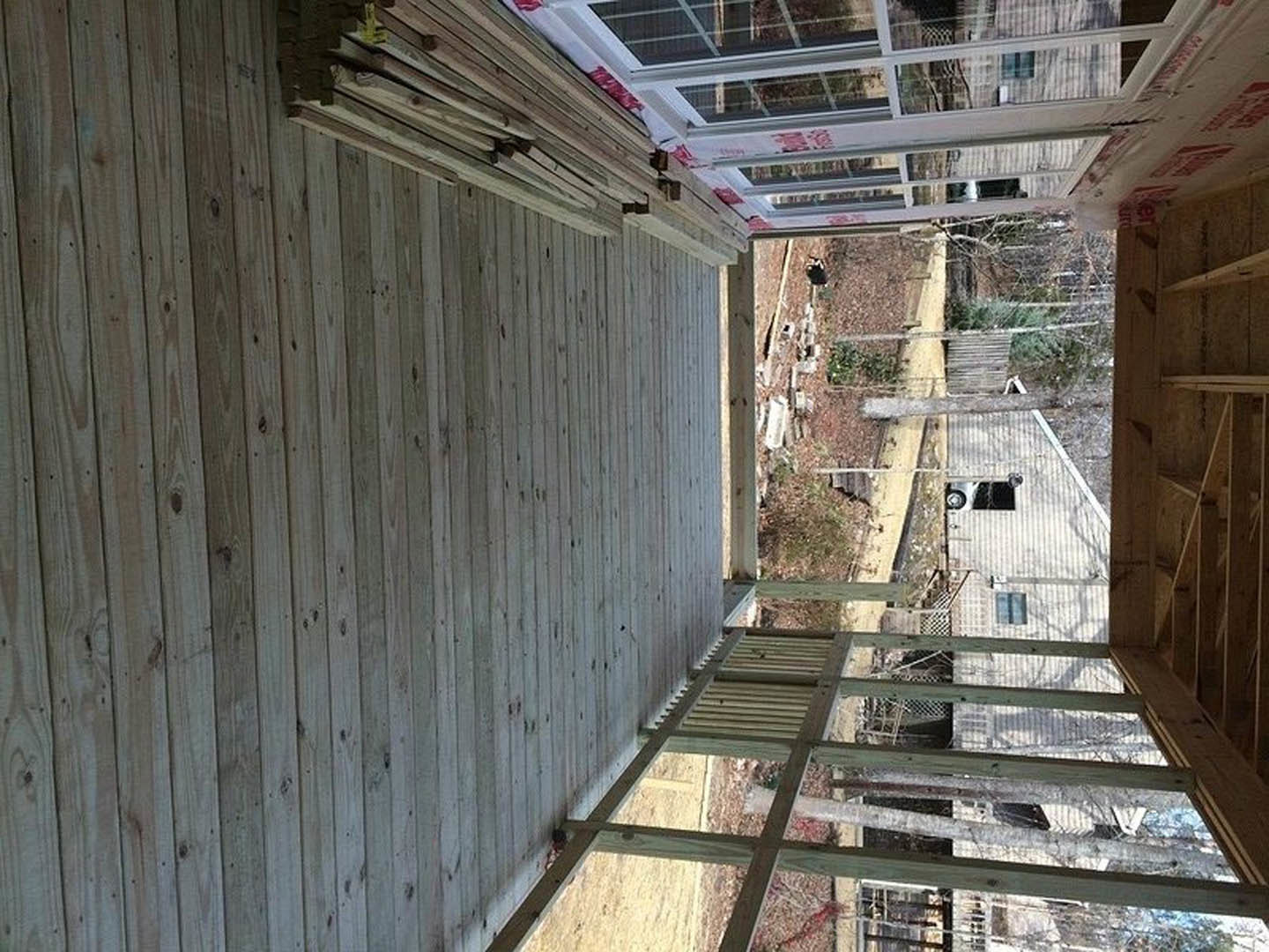 Wood plank deck with metal railing, adjacent to a modern building featuring composite siding and large windows, concrete steps leading to outdoor space