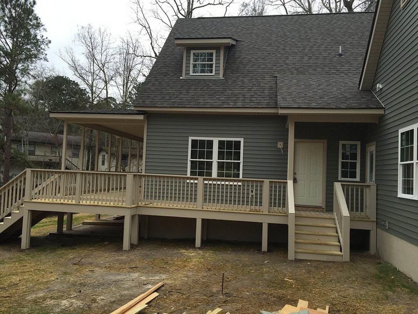 Gray siding house with white framed windows, multi-pane window, covered porch, wooden deck with railing, white door with lock, gabled roof, stairs leading to entry, surrounded by