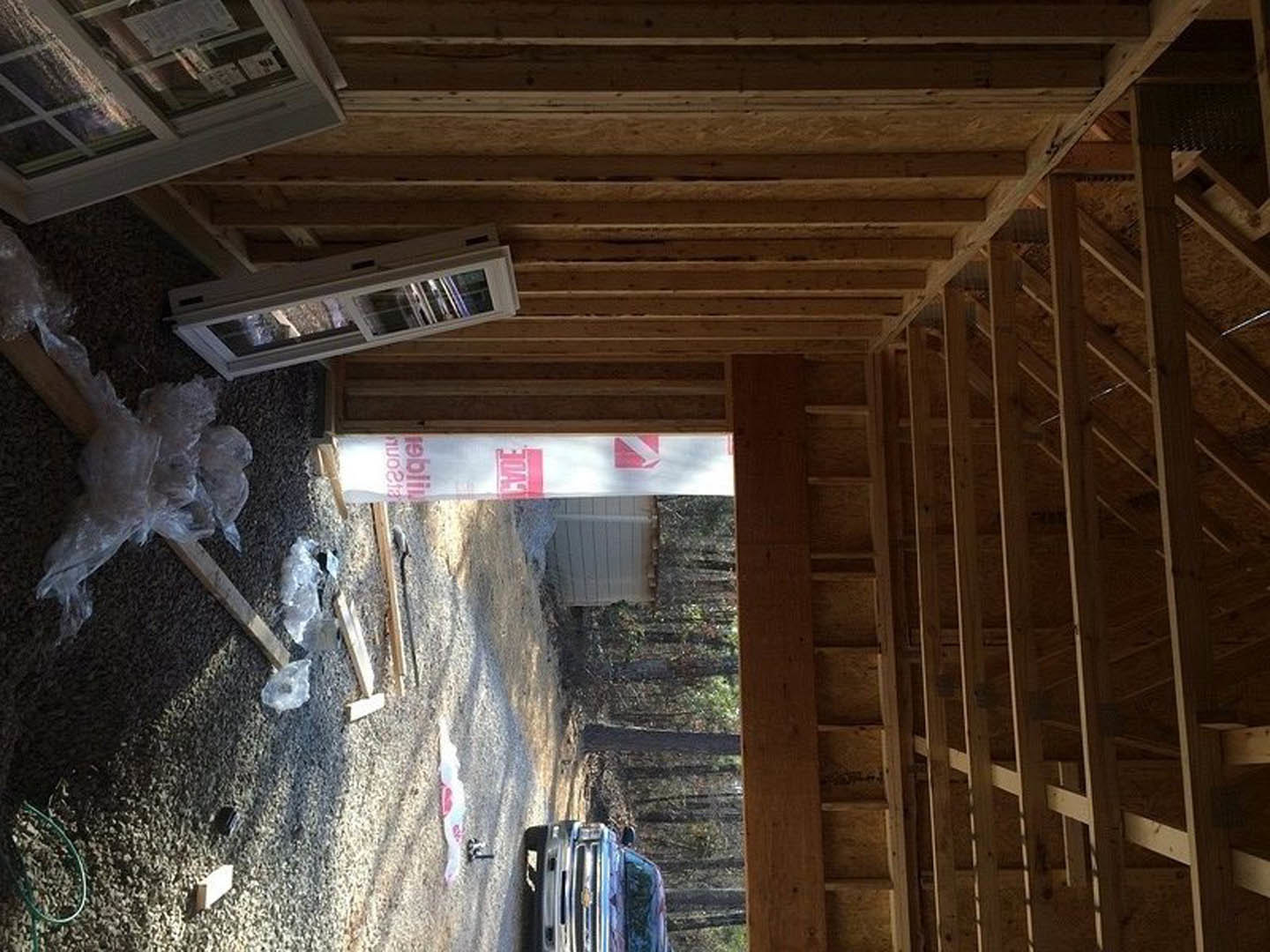 Wood-framed house under construction with exposed beams, glass window, garage opening, and construction truck parked nearby