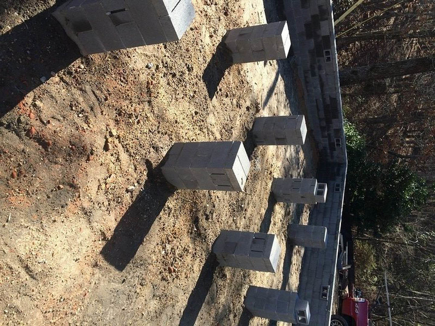 Cluster of gray concrete blocks arranged on bare dirt in a residential yard, surrounded by sparse grass and plants