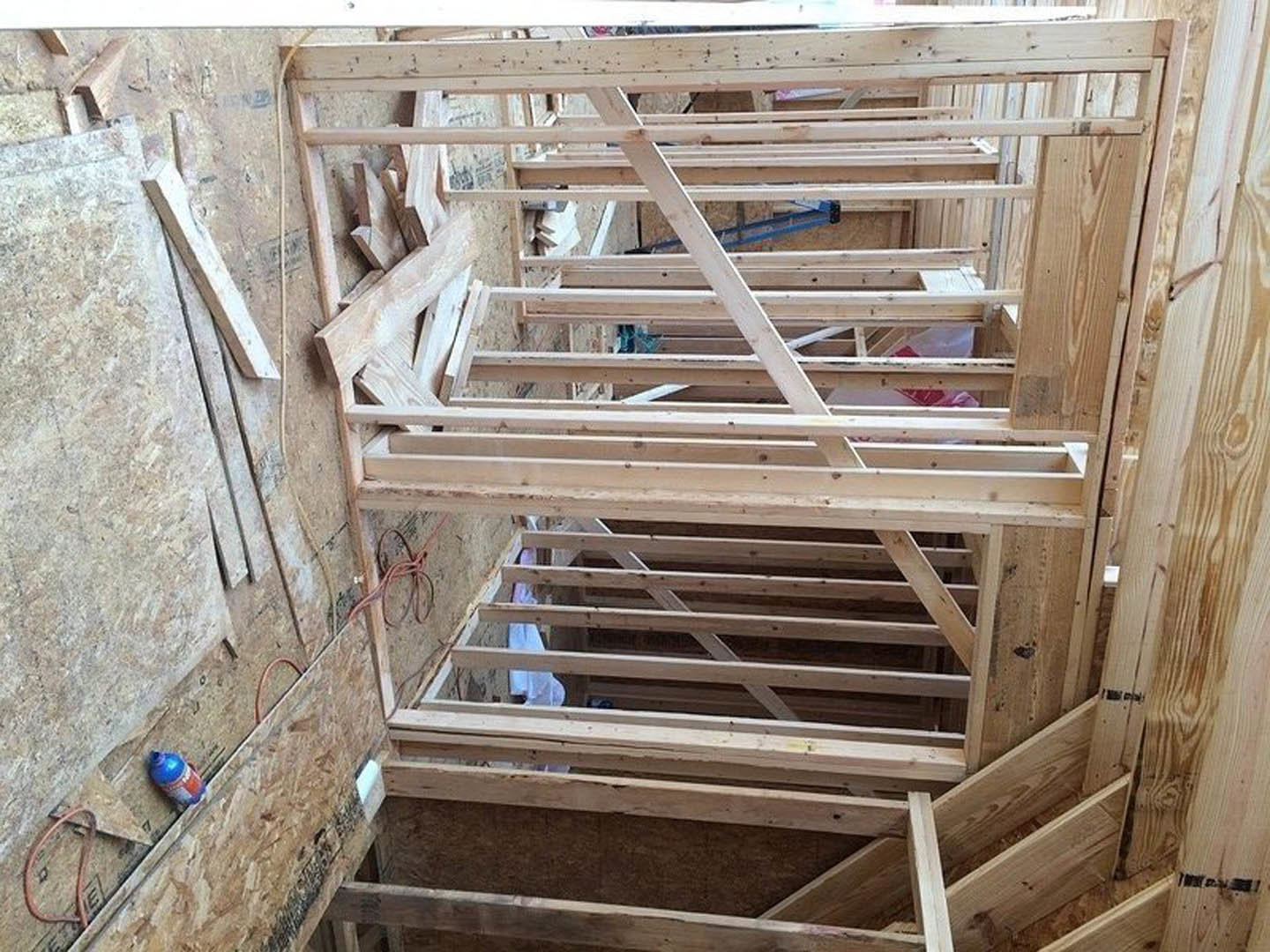 Exposed wood framing in a residential construction site with visible lumber, ladder, and unfinished walls