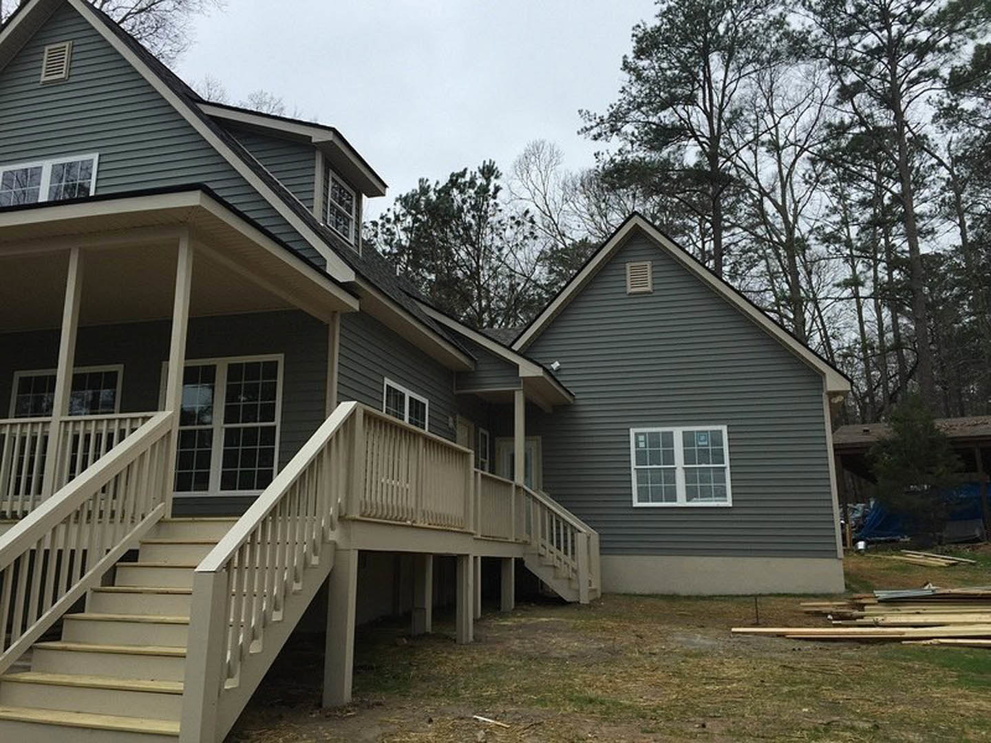 Two-story home with white-framed windows, wood siding, covered porch, and prominent exterior staircase; landscaped yard with mature tree and blue sky in background