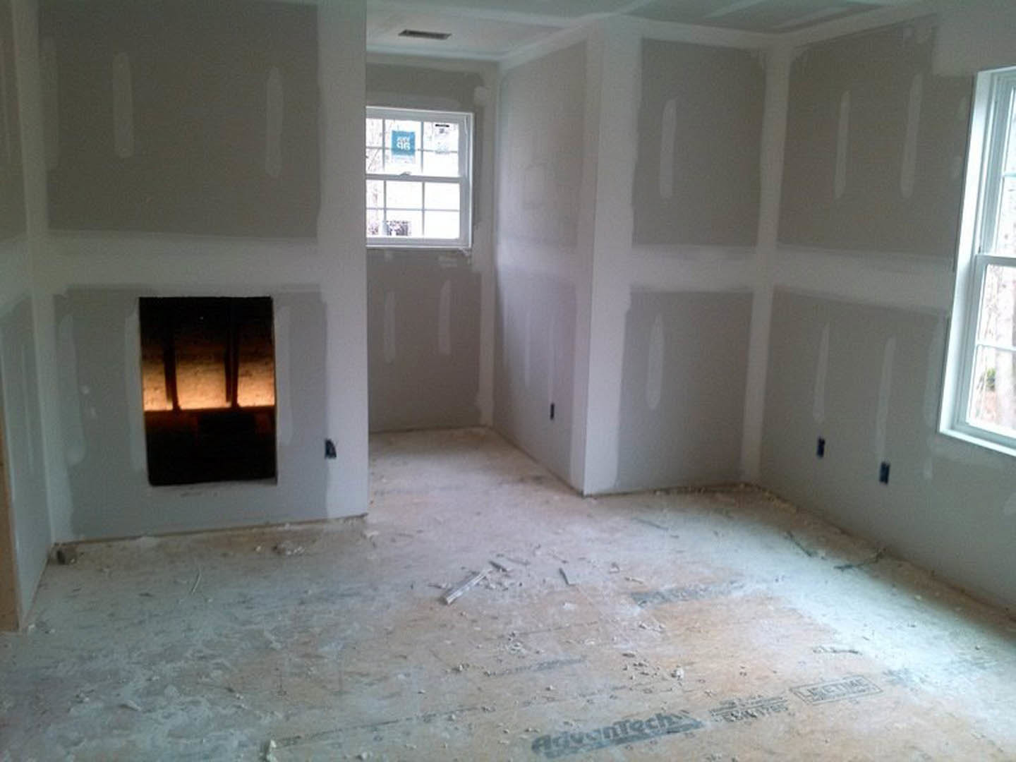 White-walled room with a window featuring a white frame, dirty floor with scattered white paint, and a close-up of a metal fixture.