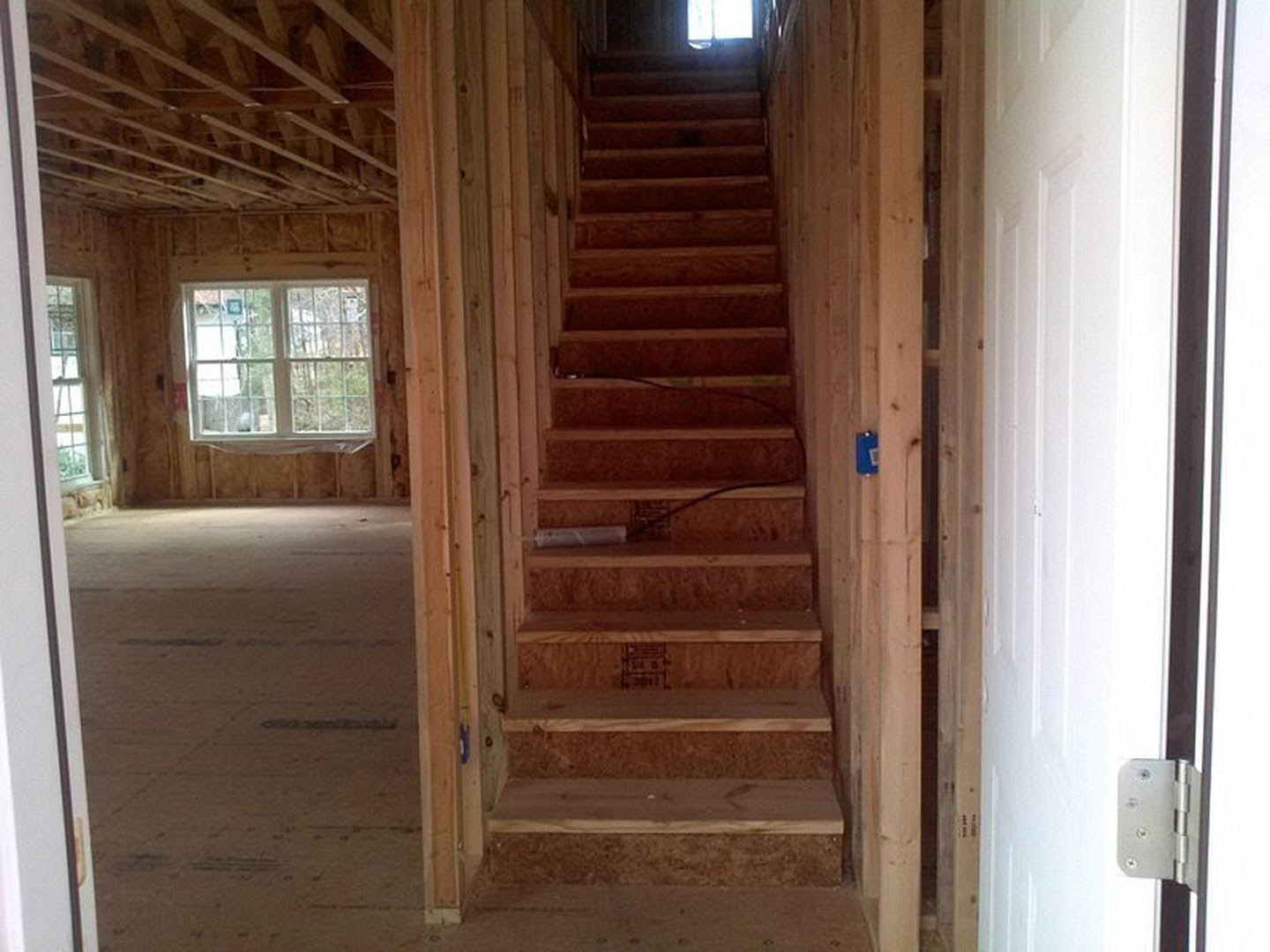 Wooden staircase with natural plank steps and white risers, large window overlooking green trees, warm-toned walls, and modern railing in residential interior.