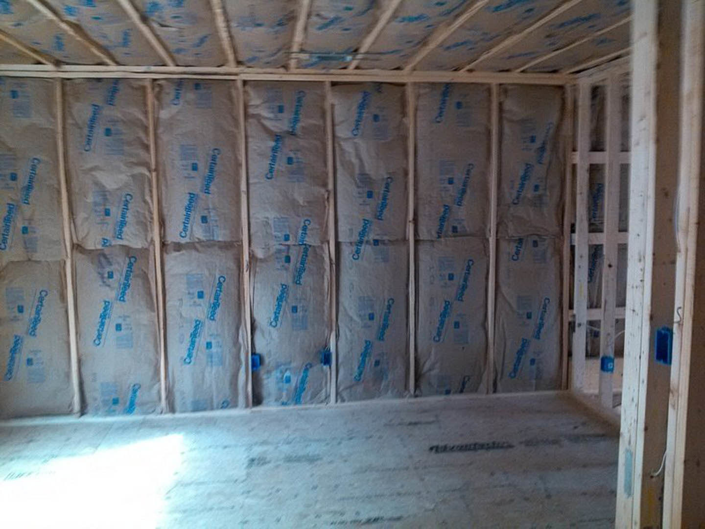 Unfinished room with exposed wall insulation, handwritten markings on insulation, and construction materials scattered on floor