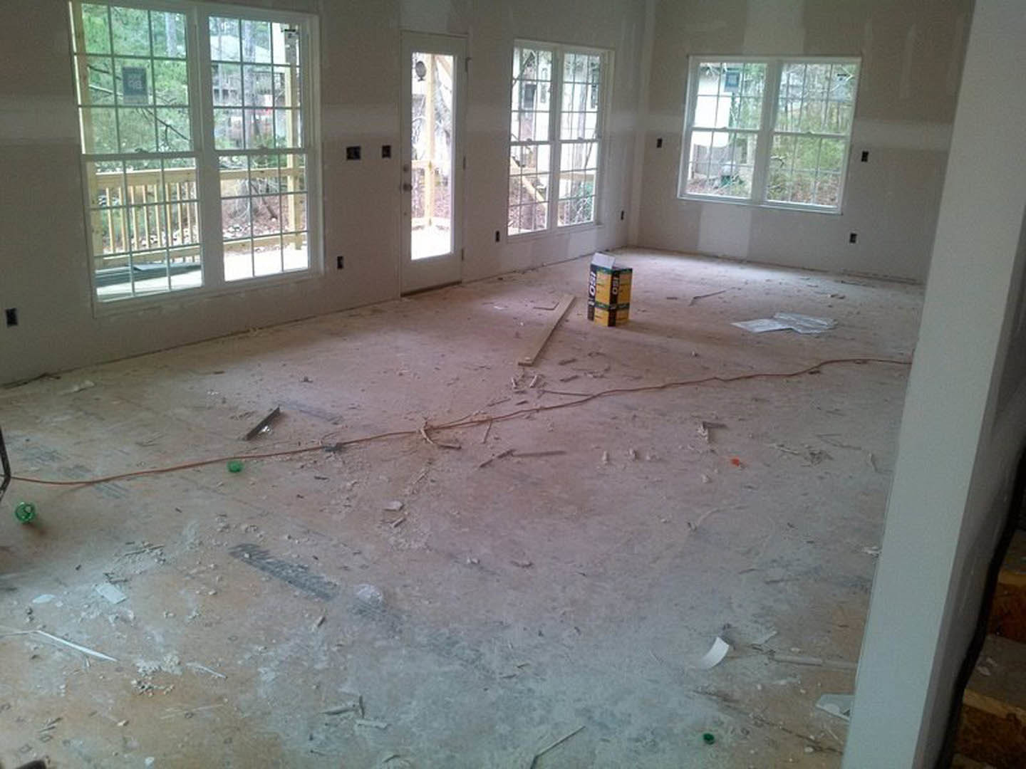 Living room with multiple large windows, light wood flooring, white plaster walls, and a yellow rectangular ottoman.