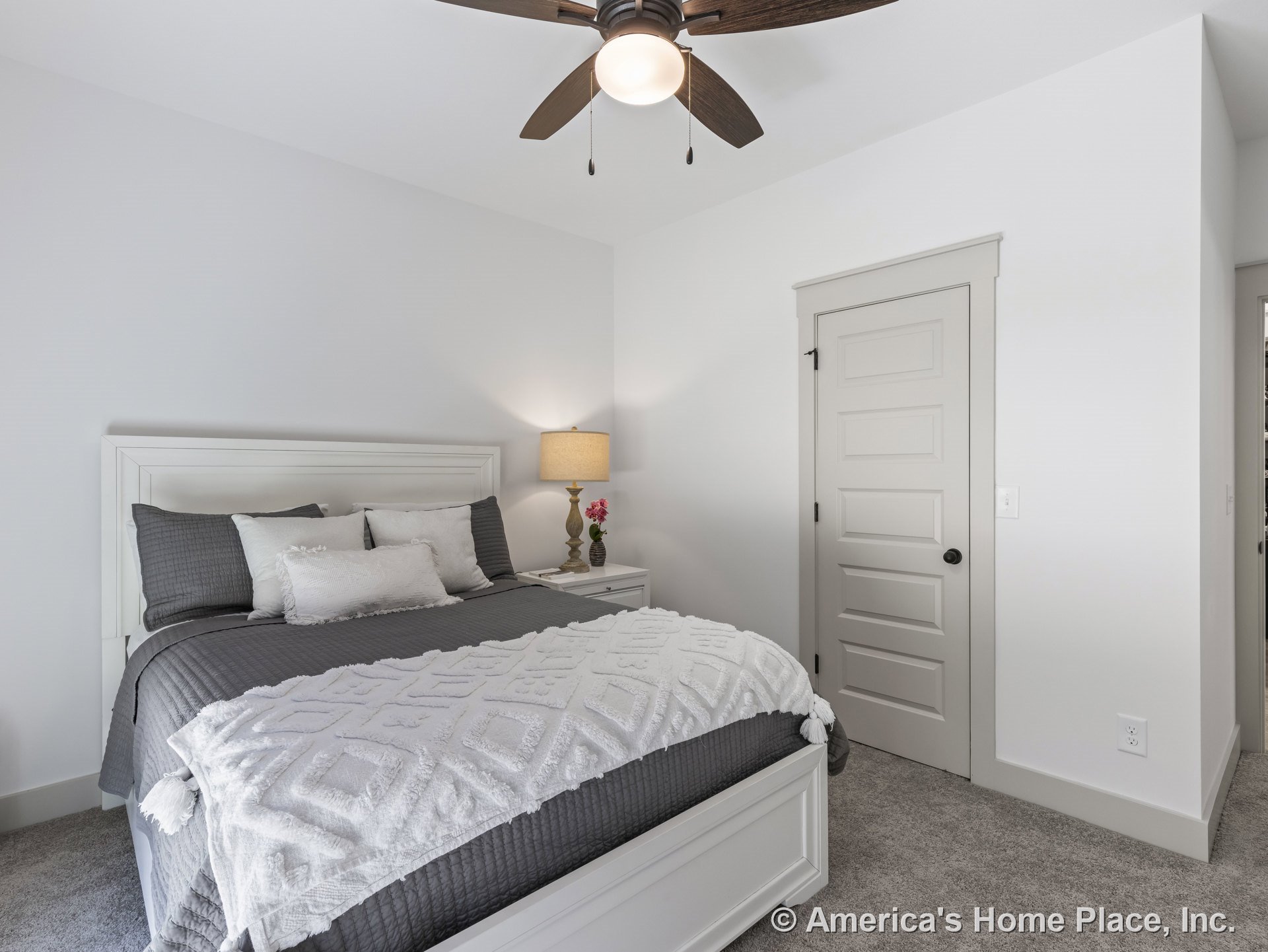 Bedroom with white paneled interior door, gray carpet flooring, white painted trim and baseboards, ceiling fan with light fixture, neutral wall color, and built-in electrical