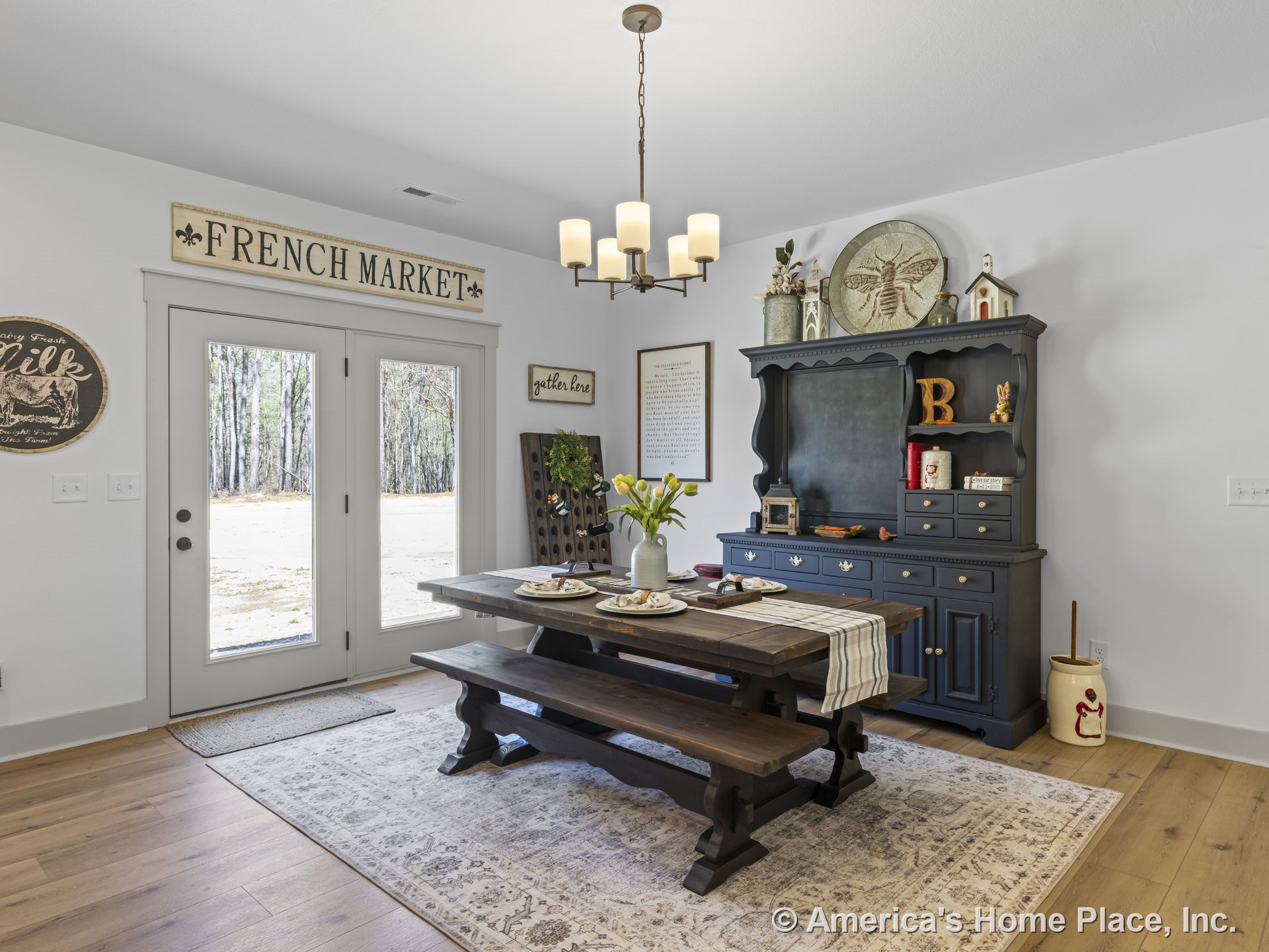 Light wood plank flooring and white painted walls frame a dining room with double glass doors trimmed in white, built-in ceiling chandelier, large black hutch cabinetry, and a
