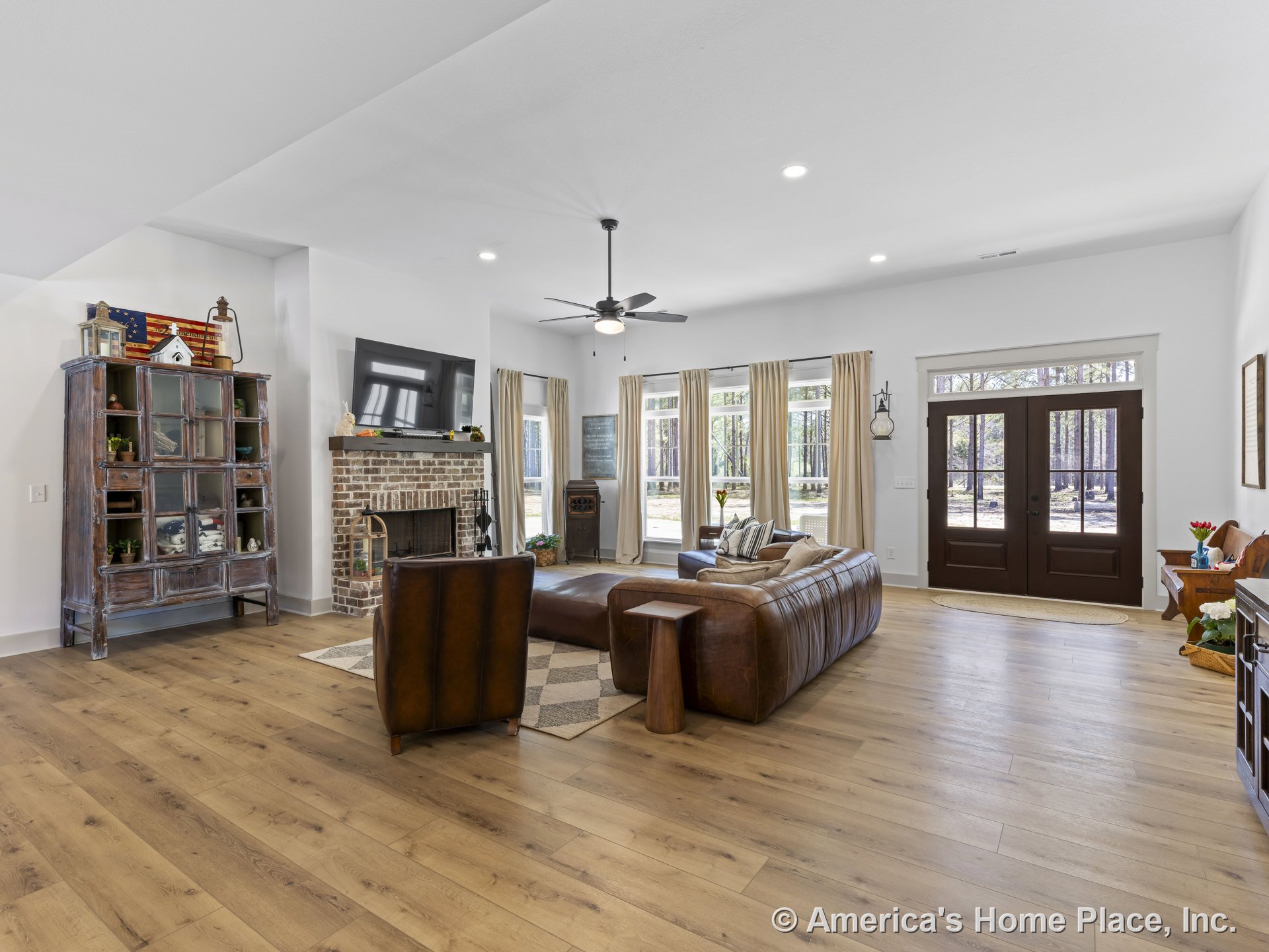 Wide plank wood flooring, brick fireplace with mantel, large windows with trim, double front entry doors, ceiling fan with light, recessed ceiling lights, open living room layout