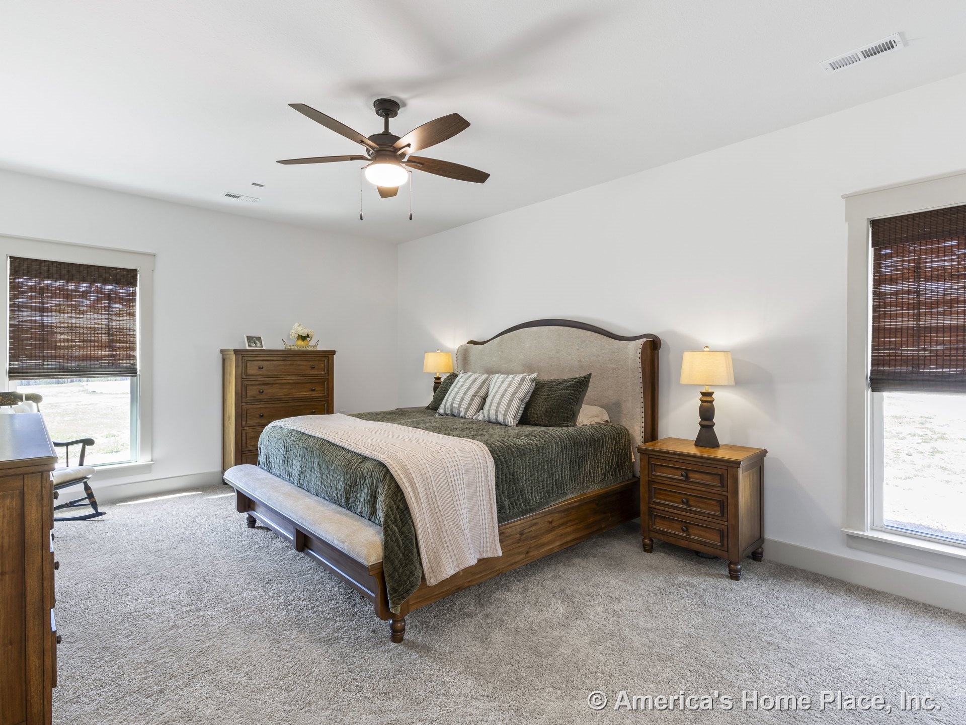 Carpeted bedroom with large windows fitted with woven shades, ceiling fan featuring built-in lighting, white trim, and neutral wall color.