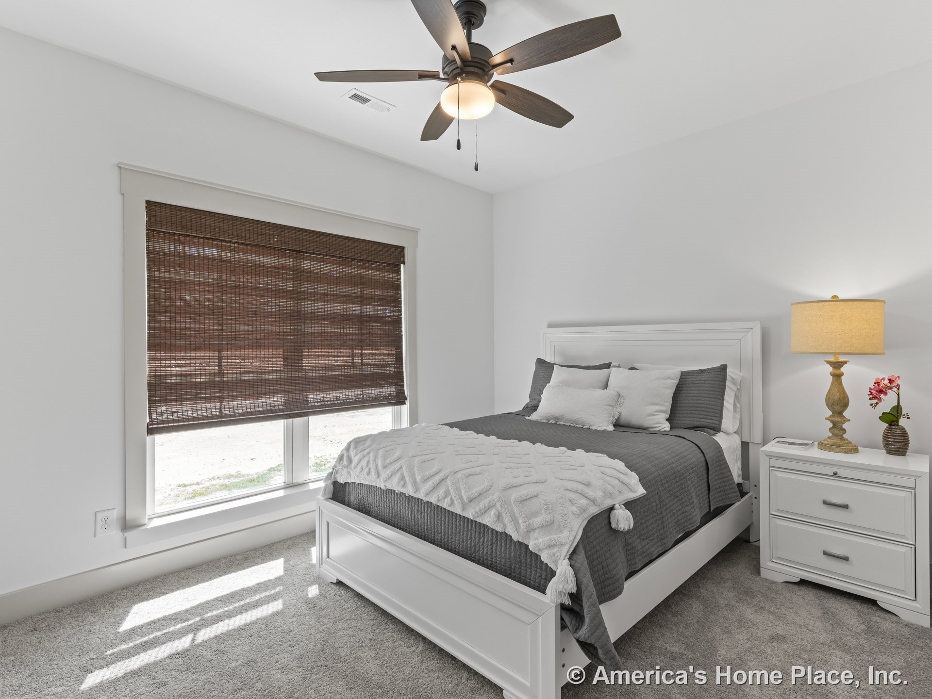 Bedroom with carpet flooring, white painted walls, large window framed in white trim, woven wood blinds, built-in window sill, and ceiling fan with integrated light fixture.