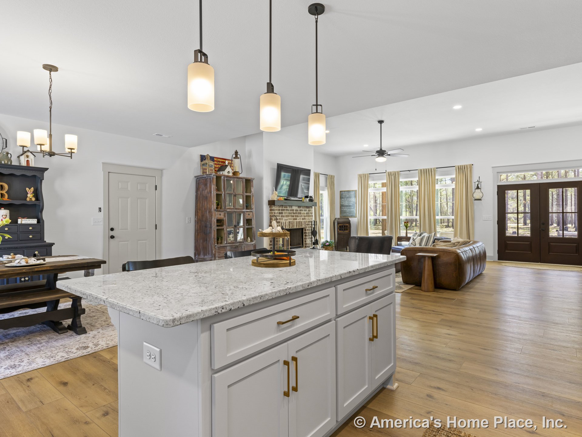 Open-concept living area with wide plank wood flooring, white shaker cabinets, quartz kitchen island, pendant lighting, brick fireplace with mantel, large windows with trim, dining