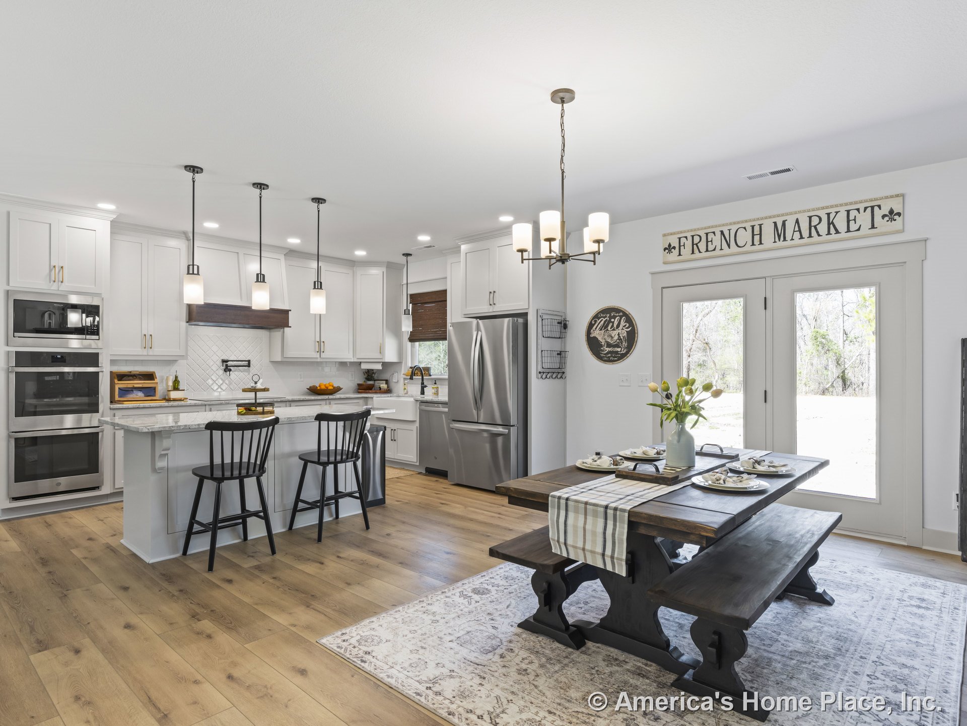 White shaker cabinets and marble kitchen island with built-in double ovens, pendant lights, tile backsplash, wood plank flooring, and adjacent dining area featuring double glass
