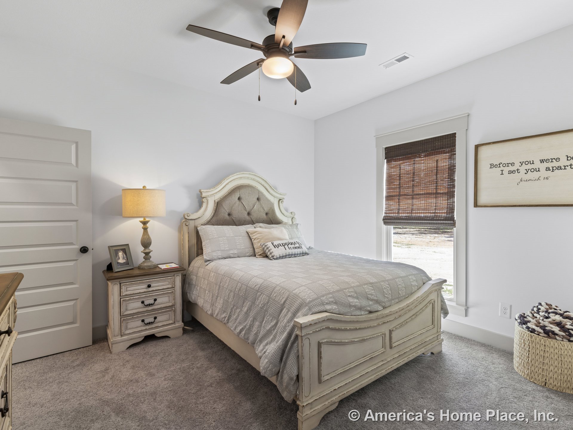 Carpeted bedroom with white painted walls, ceiling fan with integrated light, window framed by traditional trim and woven wood blinds, paneled interior door, baseboard molding, and
