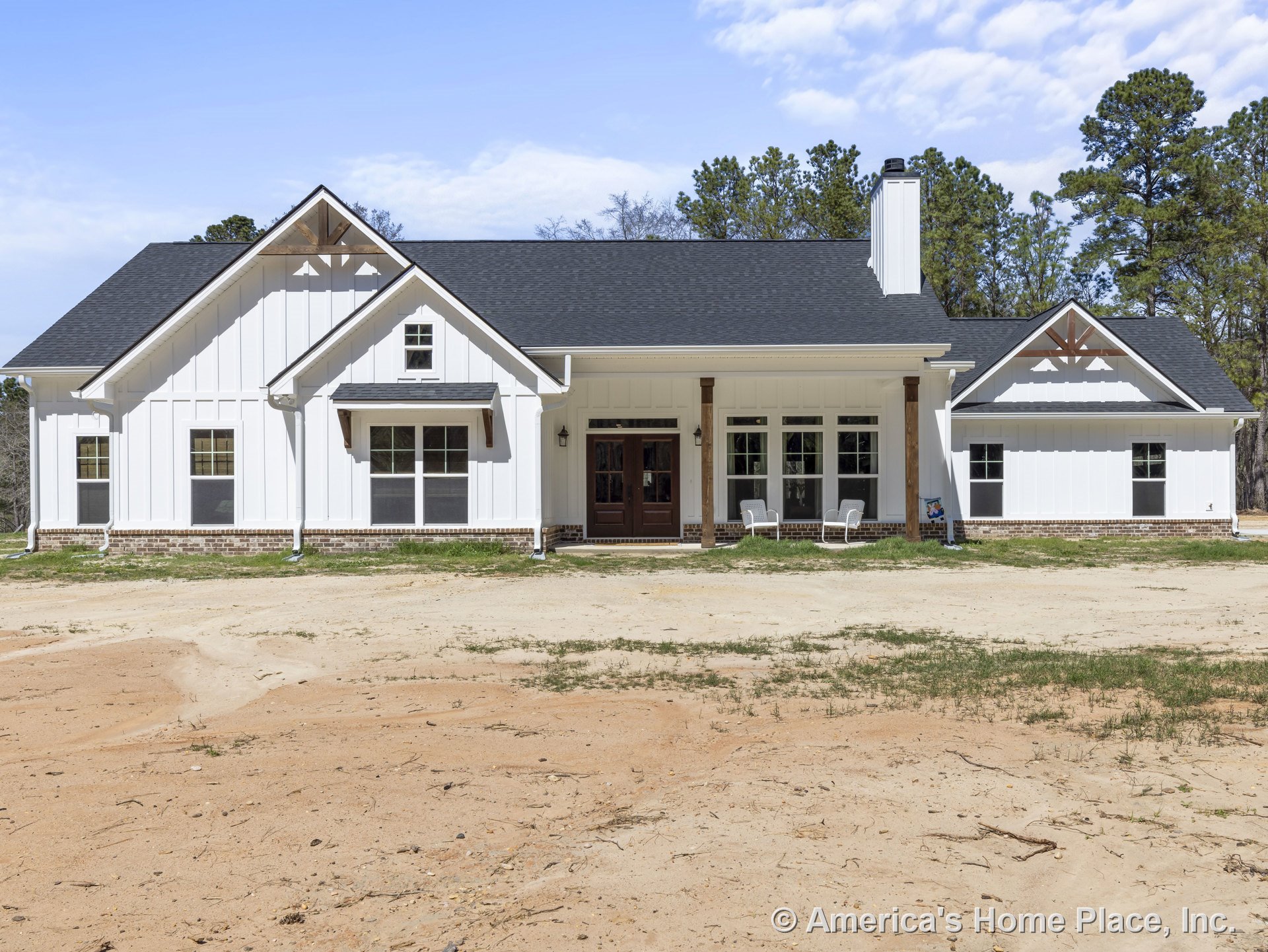White board and batten siding with brick foundation trim, covered front porch supported by wood columns, multiple front windows, gable roof featuring decorative trusses.
