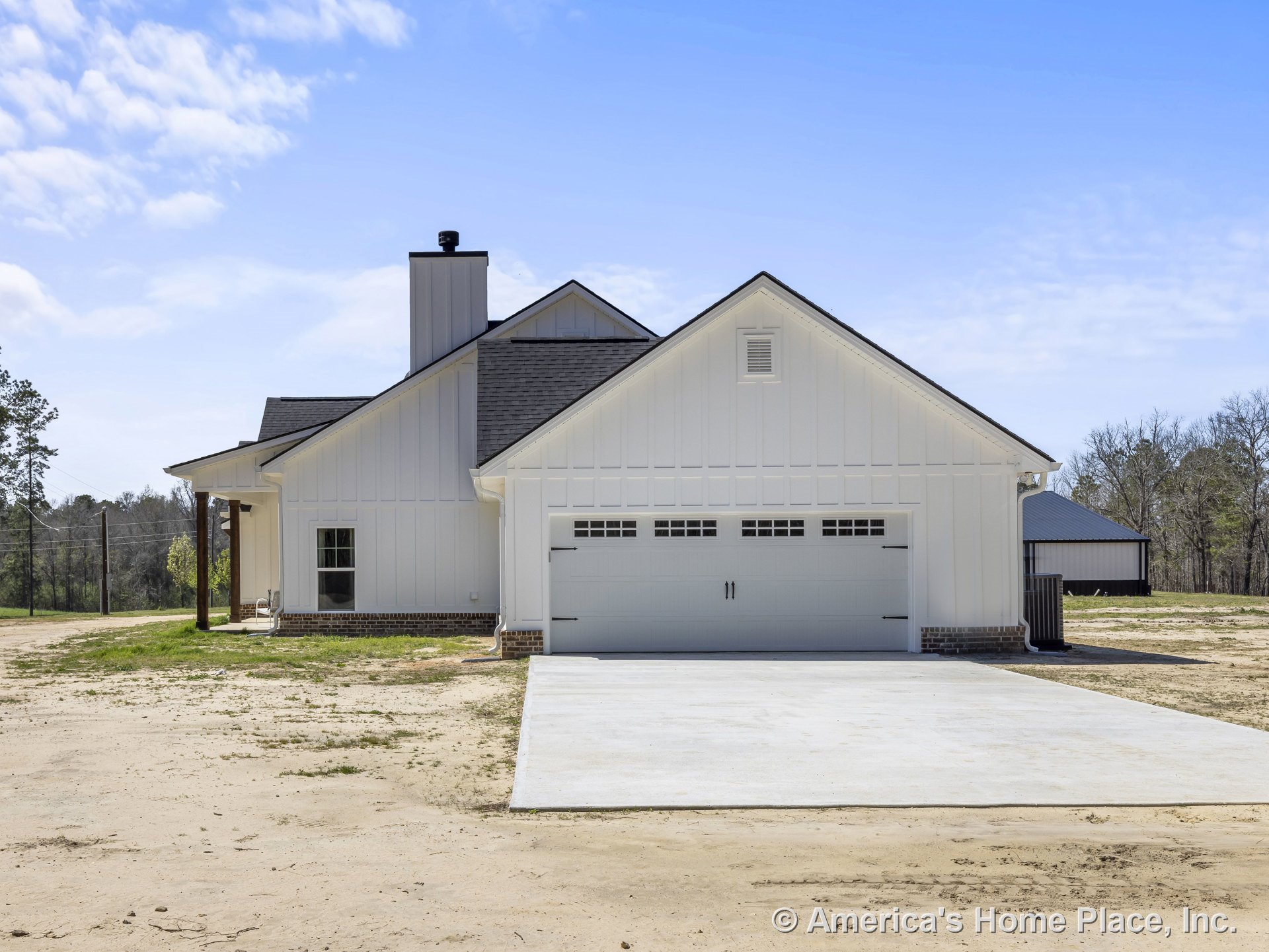 White board and batten siding with brick foundation trim, two-car garage door, concrete driveway, covered porch entry, prominent chimney, farmhouse-style roof, and multiple