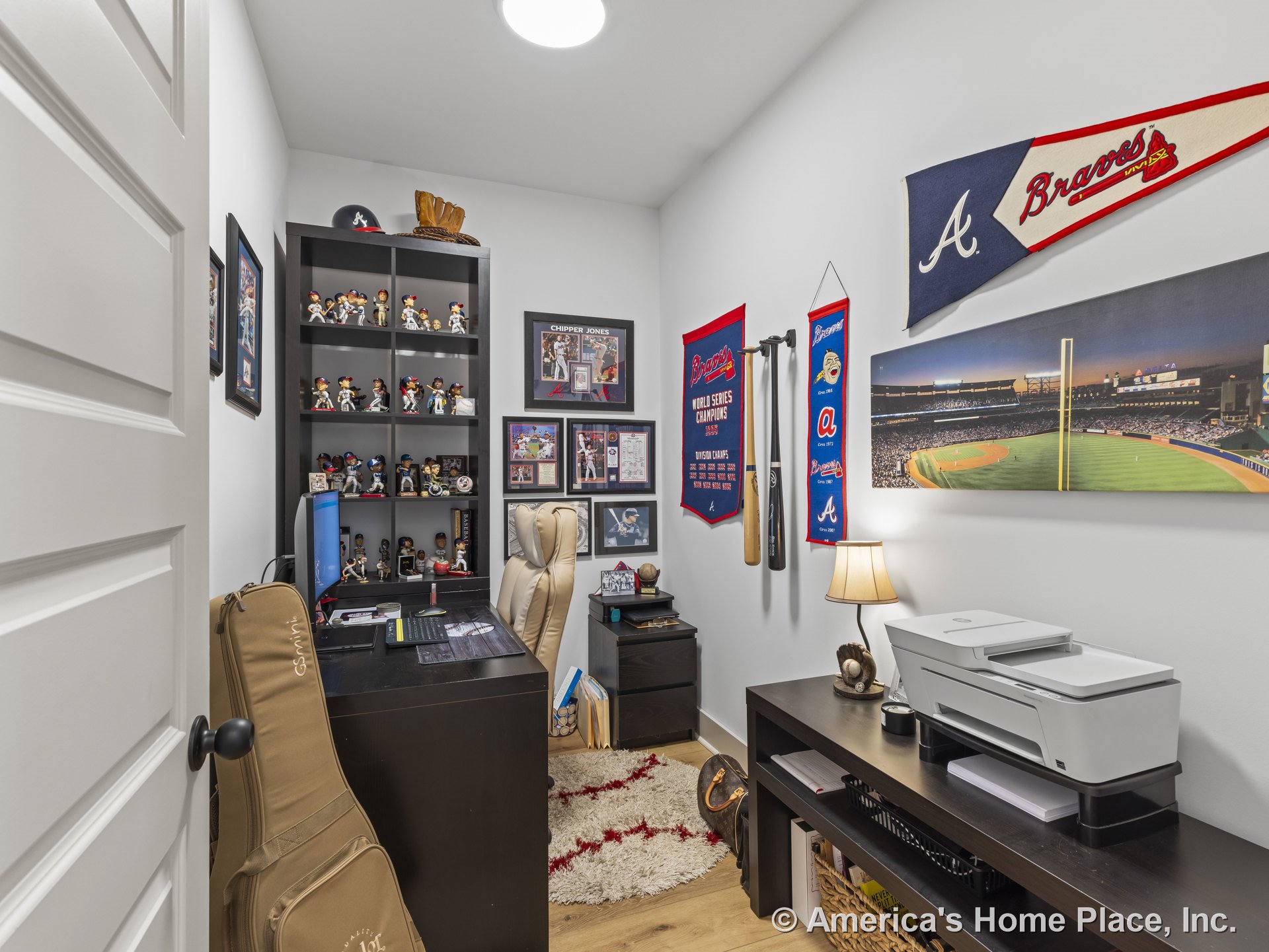 Built-in shelving unit along one wall, wood plank flooring, recessed ceiling light, white paneled door, wall trim, compact printer station and desk in a small home office with