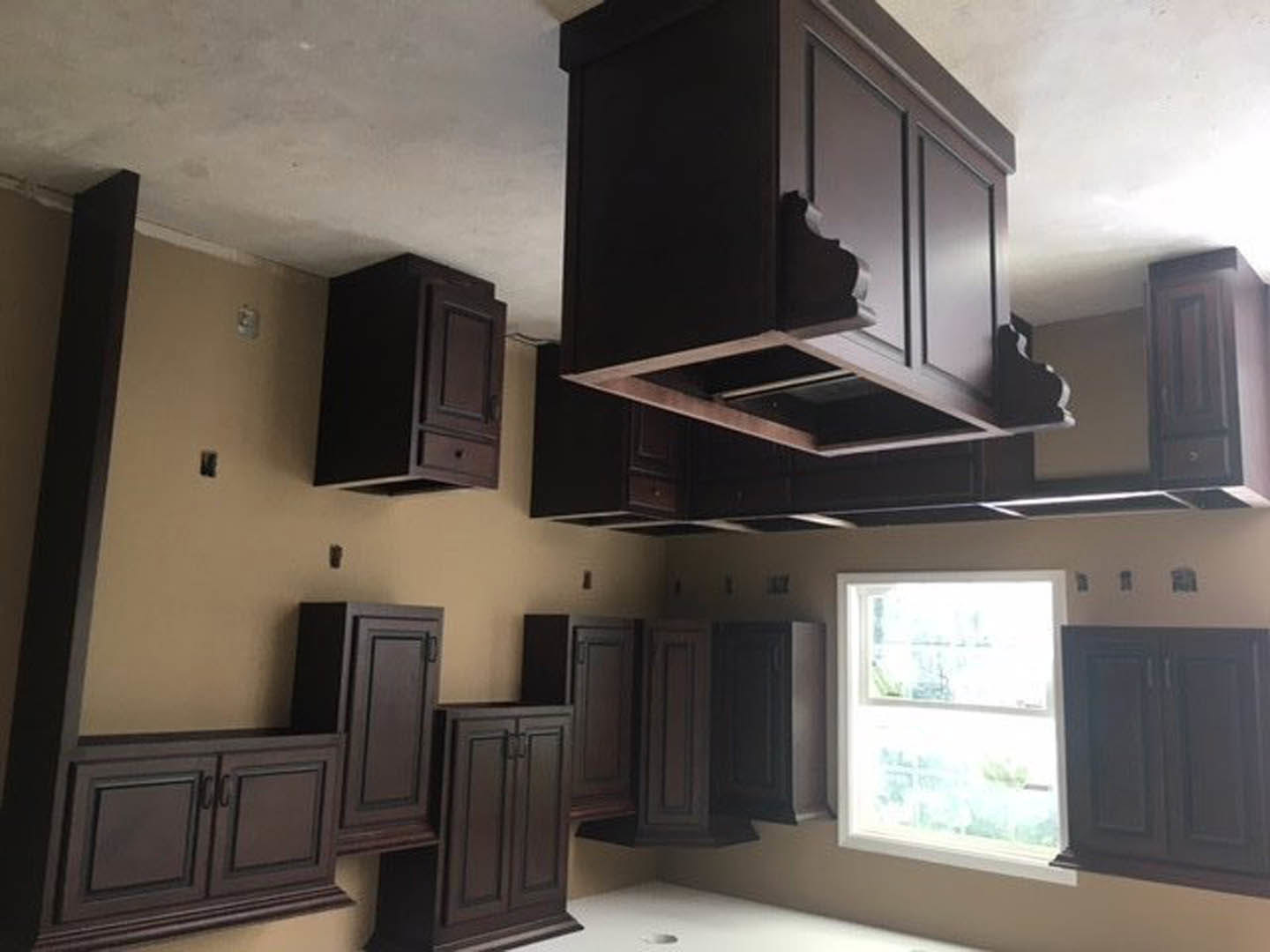 Kitchen with dark wood cabinets, black range hood, white countertops, and large window letting in natural light